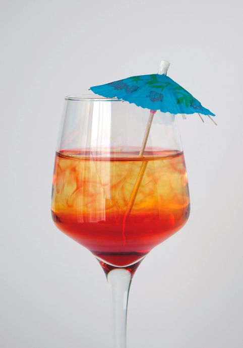 Cocktail in a glass with layered red and yellow liquid, garnished with a blue paper umbrella.