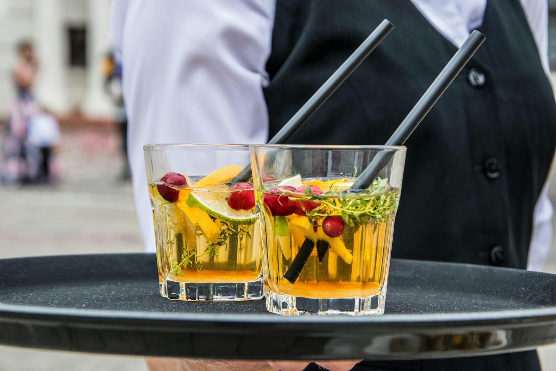 Waiter holding a tray with two cocktails garnished with fruit and straws.