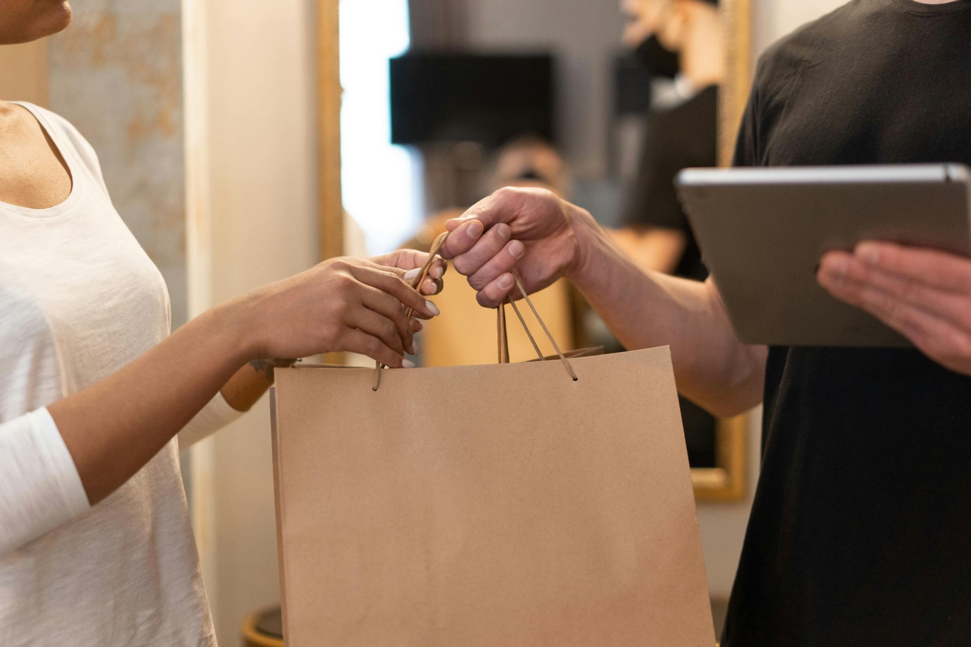 A person receiving a brown paper bag from a delivery person holding a tablet. Indoors.