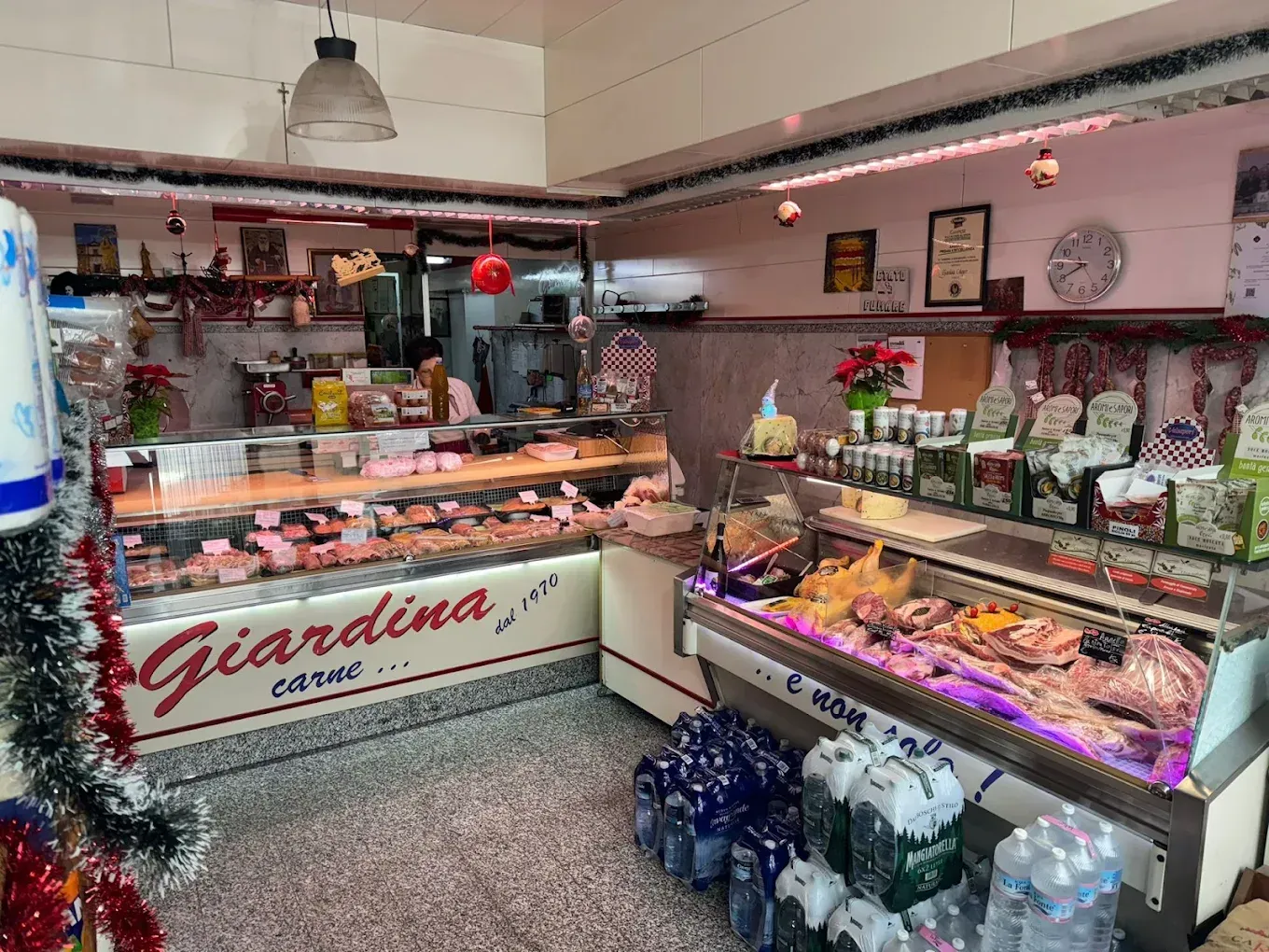 Interno di una macelleria con vetrine piene di carne e prodotti confezionati. Decorazioni rosse e verdi.