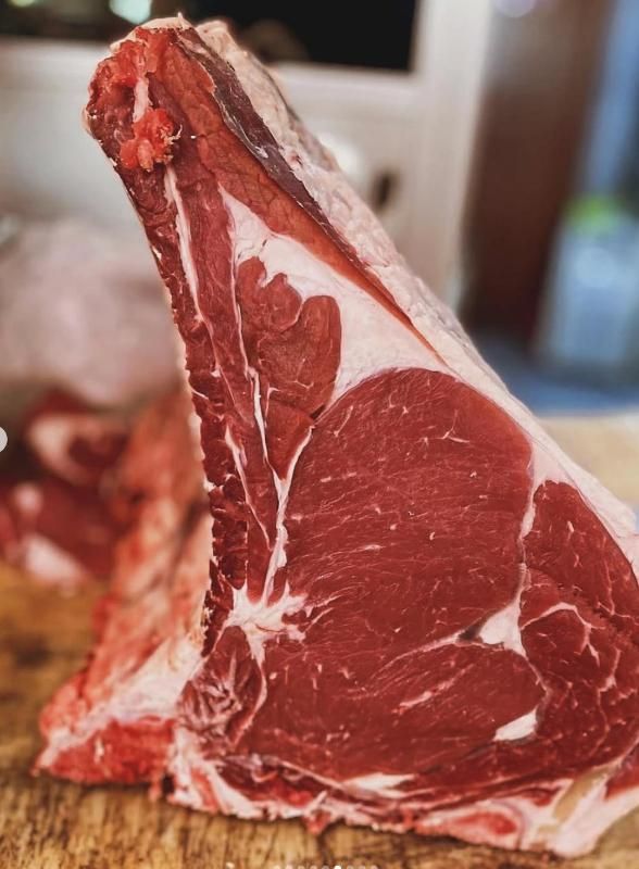 Bistecca di ribeye cruda con osso su una superficie di legno, che mostra la carne rossa e il grasso bianco.