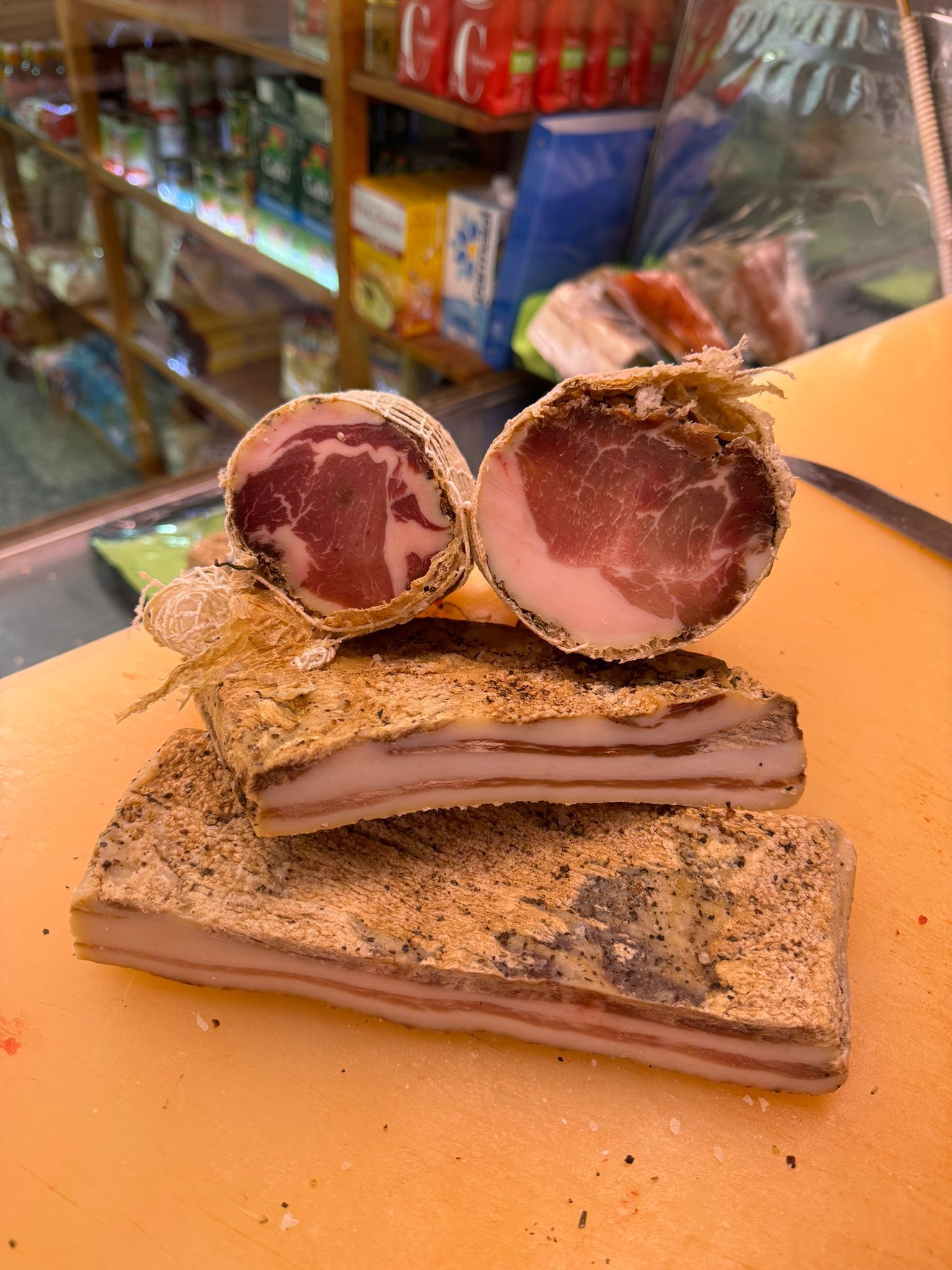 Fette di carne stagionata, tra cui un taglio rotondo, su un tagliere, con uno sfondo sfocato da supermercato.