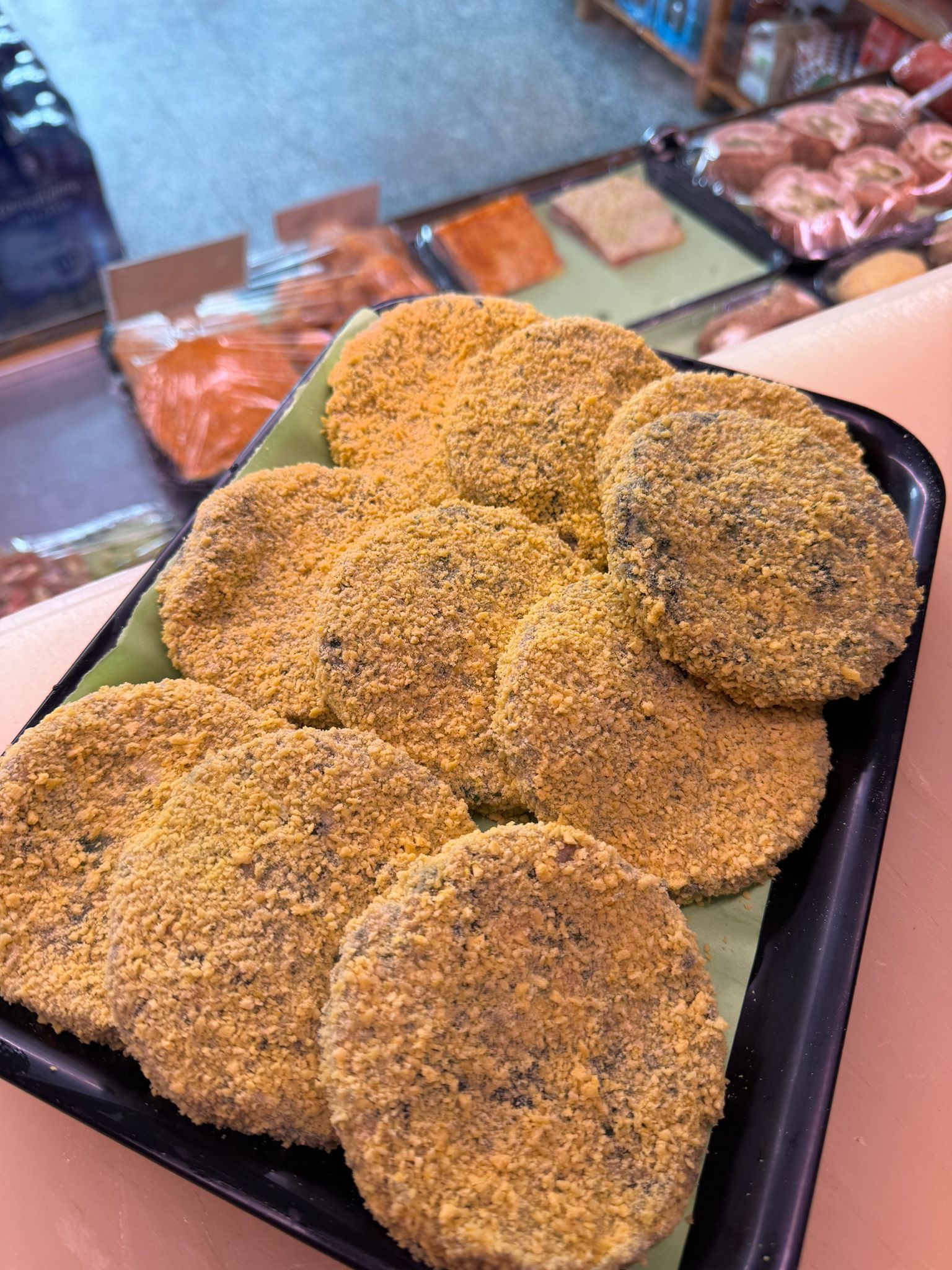 Vassoio di alimenti rotondi e impanati, possibilmente polpette o cotolette, su un bancone.