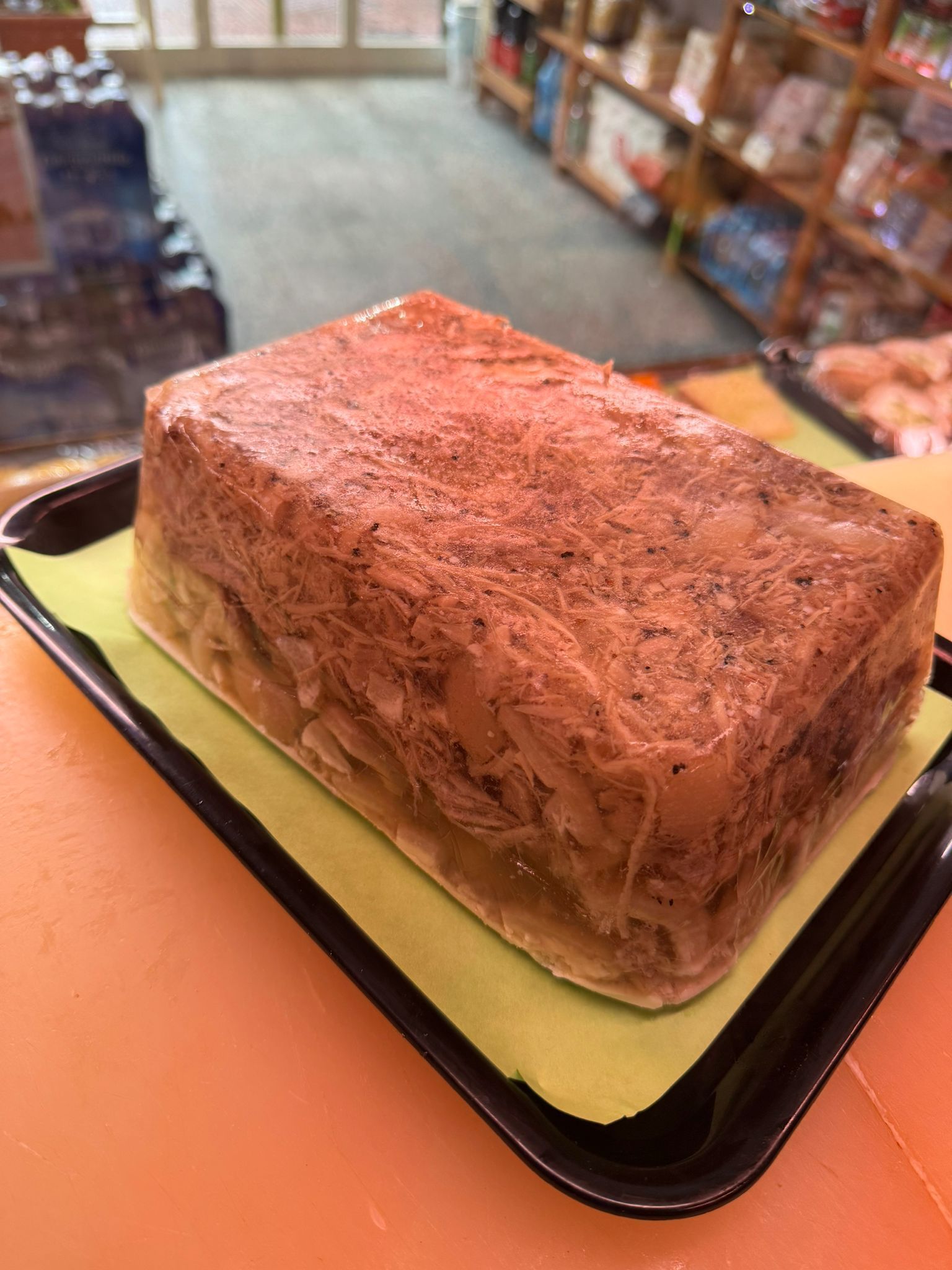 Blocco rettangolare di cibo, probabilmente gelatina, su un vassoio nero con un rivestimento verde.