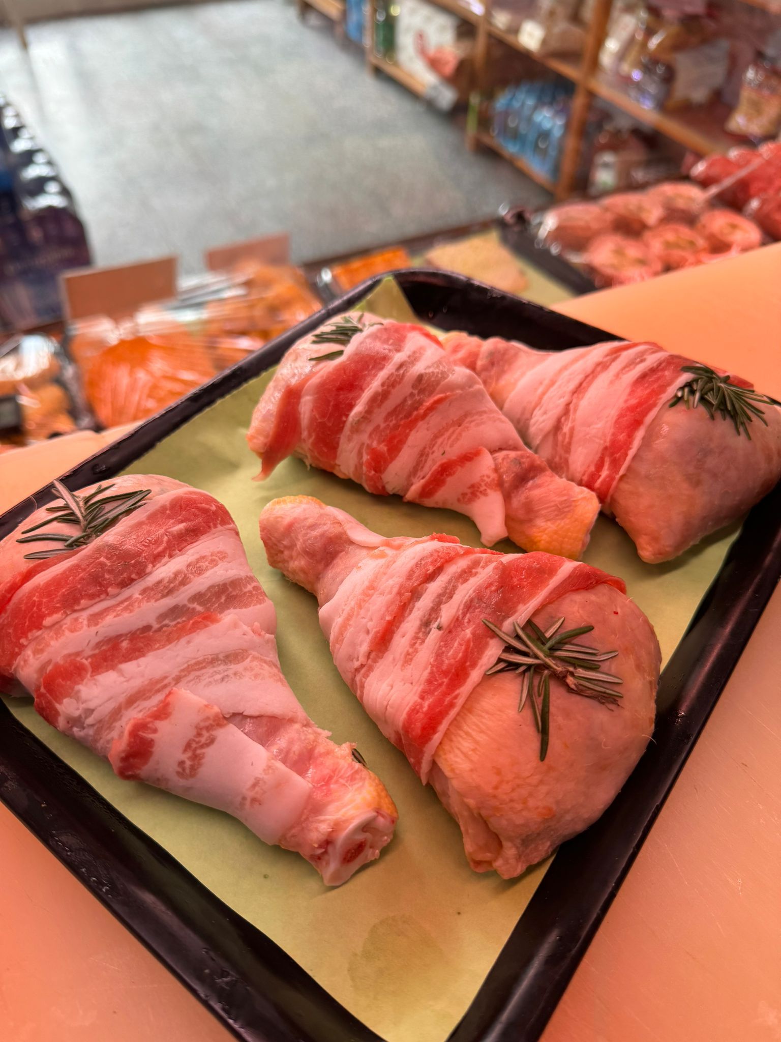 Cosce di pollo avvolte nella pancetta su un vassoio, con un rametto di rosmarino su ciascuna.