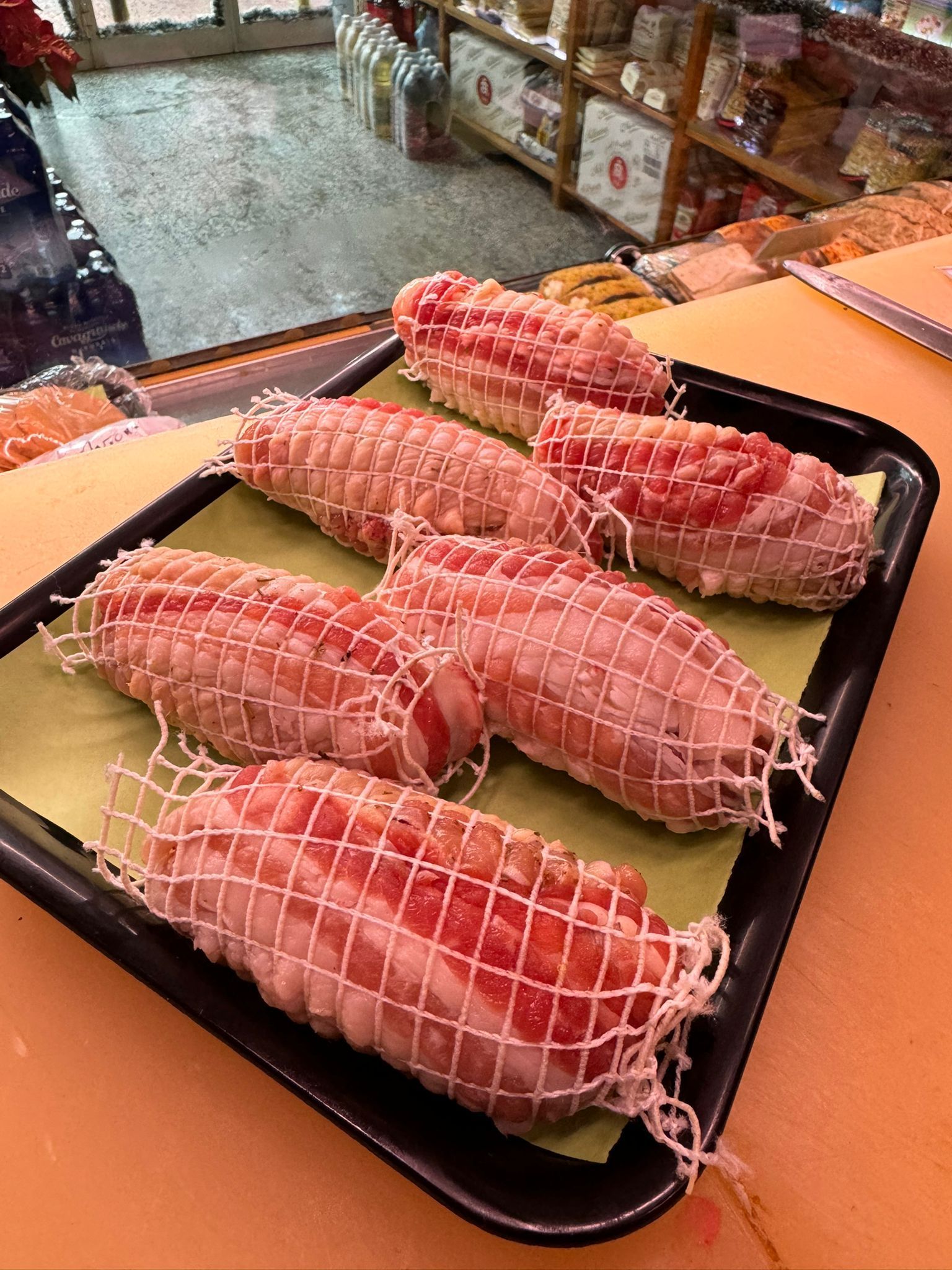Involtini di carne crudi, legati in una rete, su un vassoio nero, appoggiati su carta gialla.