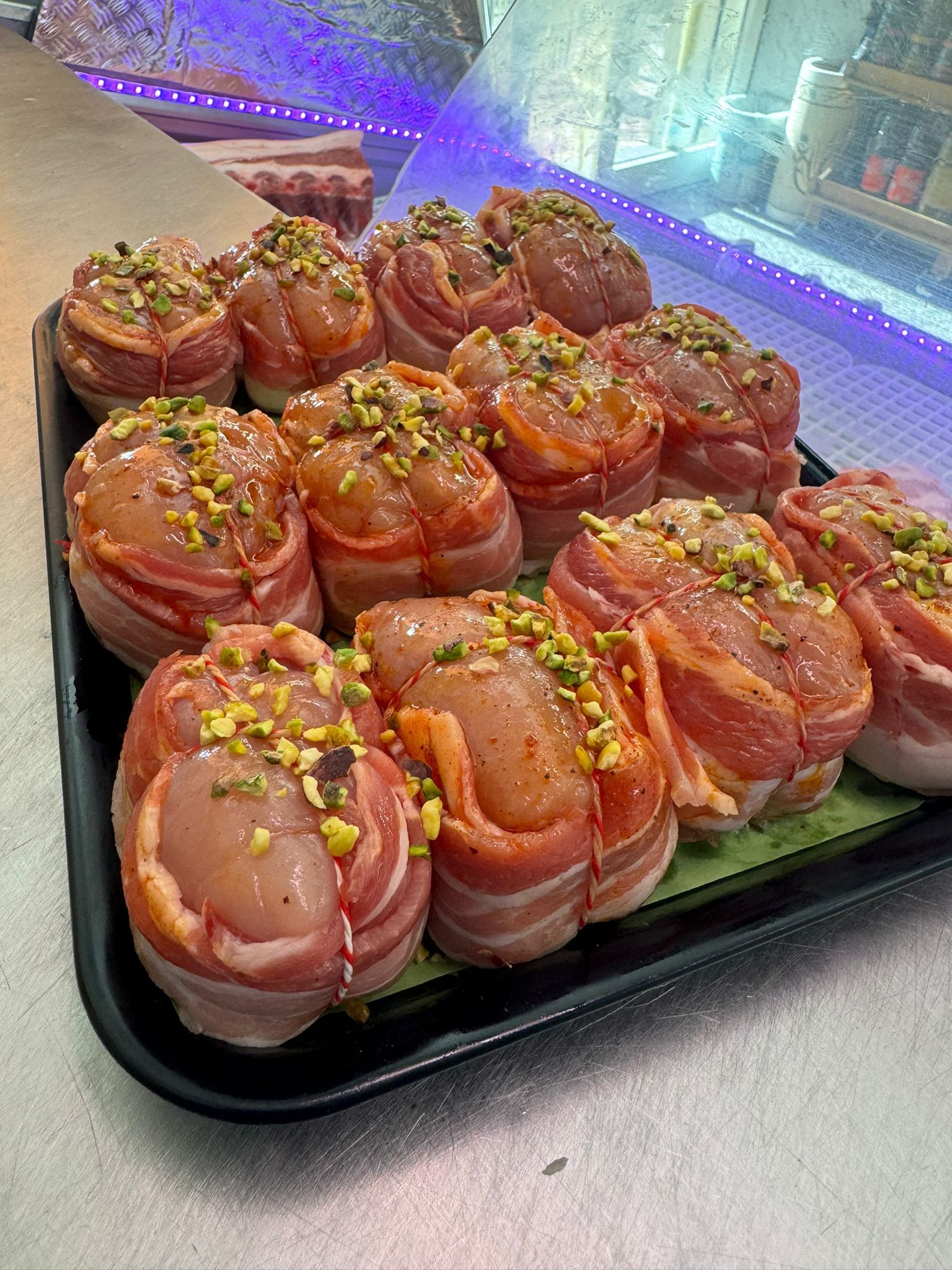 Vassoio di petti di pollo avvolti nella pancetta, guarnito con noci tritate, all'interno di una vetrina gastronomica.