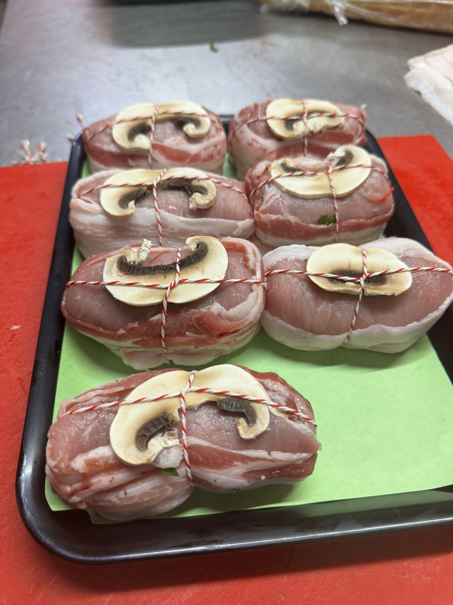 Vassoio di medaglioni di maiale avvolti nella pancetta, guarniti con funghi e legati con lo spago.