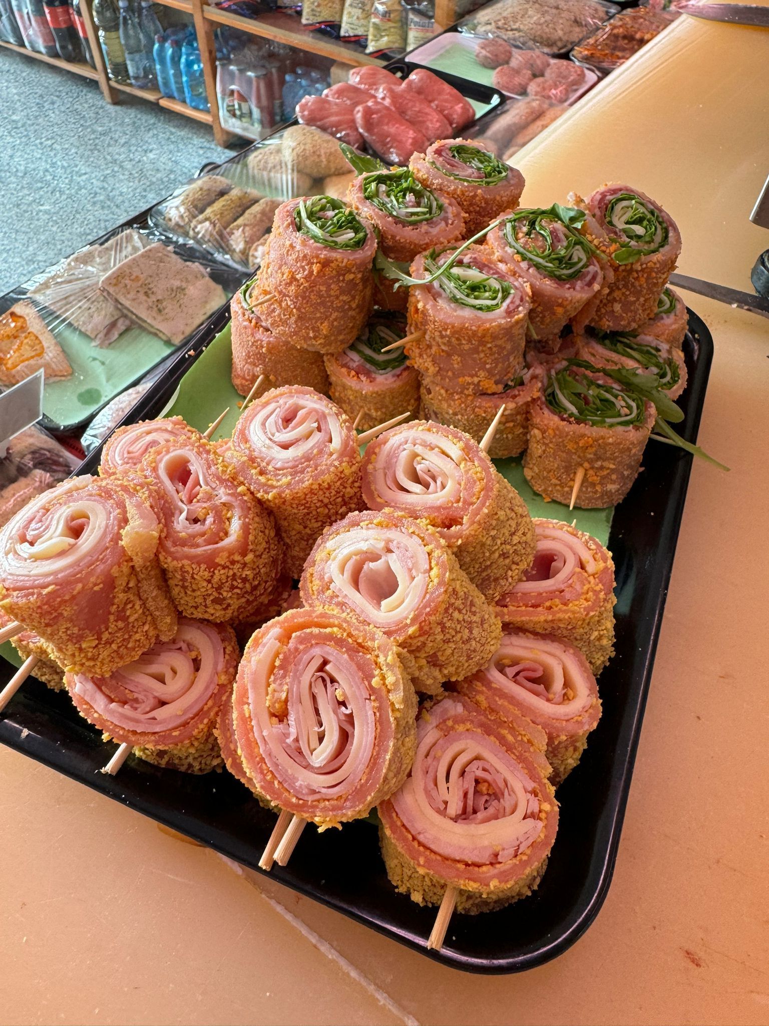 Vassoio di panini con prosciutto, formaggio e verdure infilzati su spiedini, esposti in un mercato.