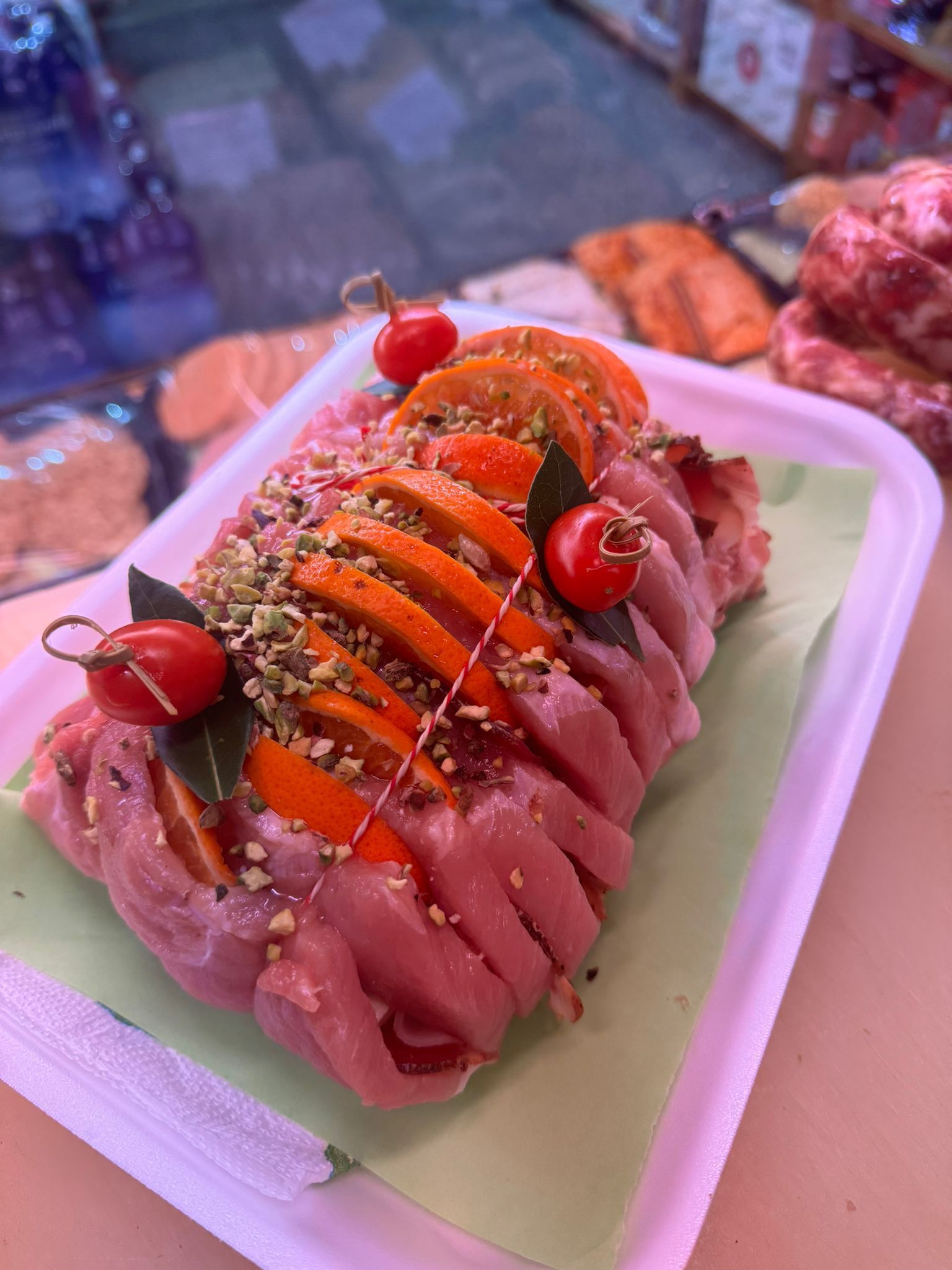 Arrosto di maiale con pomodori e pistacchi su un vassoio nero, costine avvolte in un foglio di alluminio.