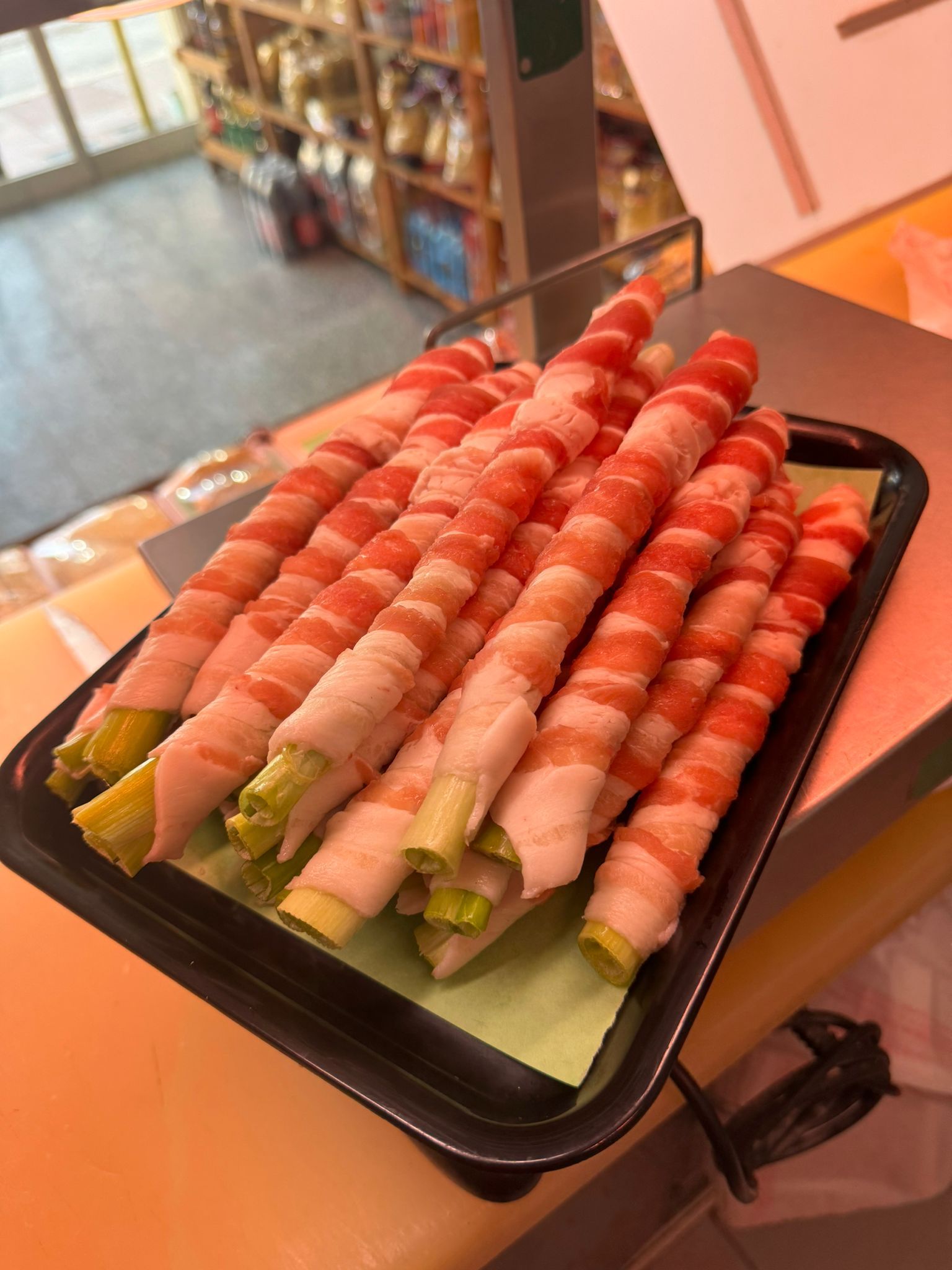 Gambi di asparagi avvolti in pancetta cruda su un vassoio nero, probabilmente in vendita al mercato.