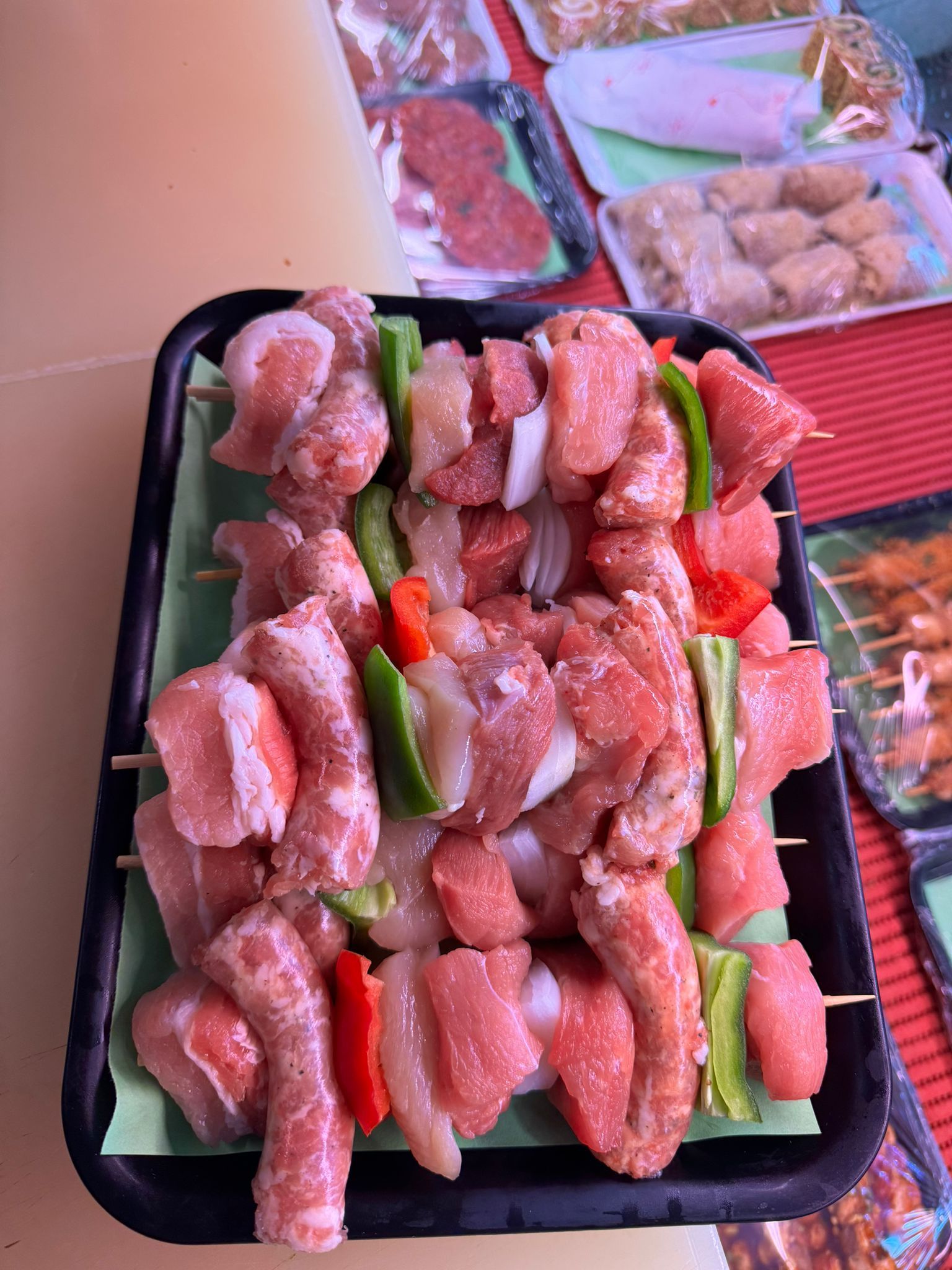 Carne cruda e verdure infilzate su un vassoio, probabilmente preparate per essere grigliate.