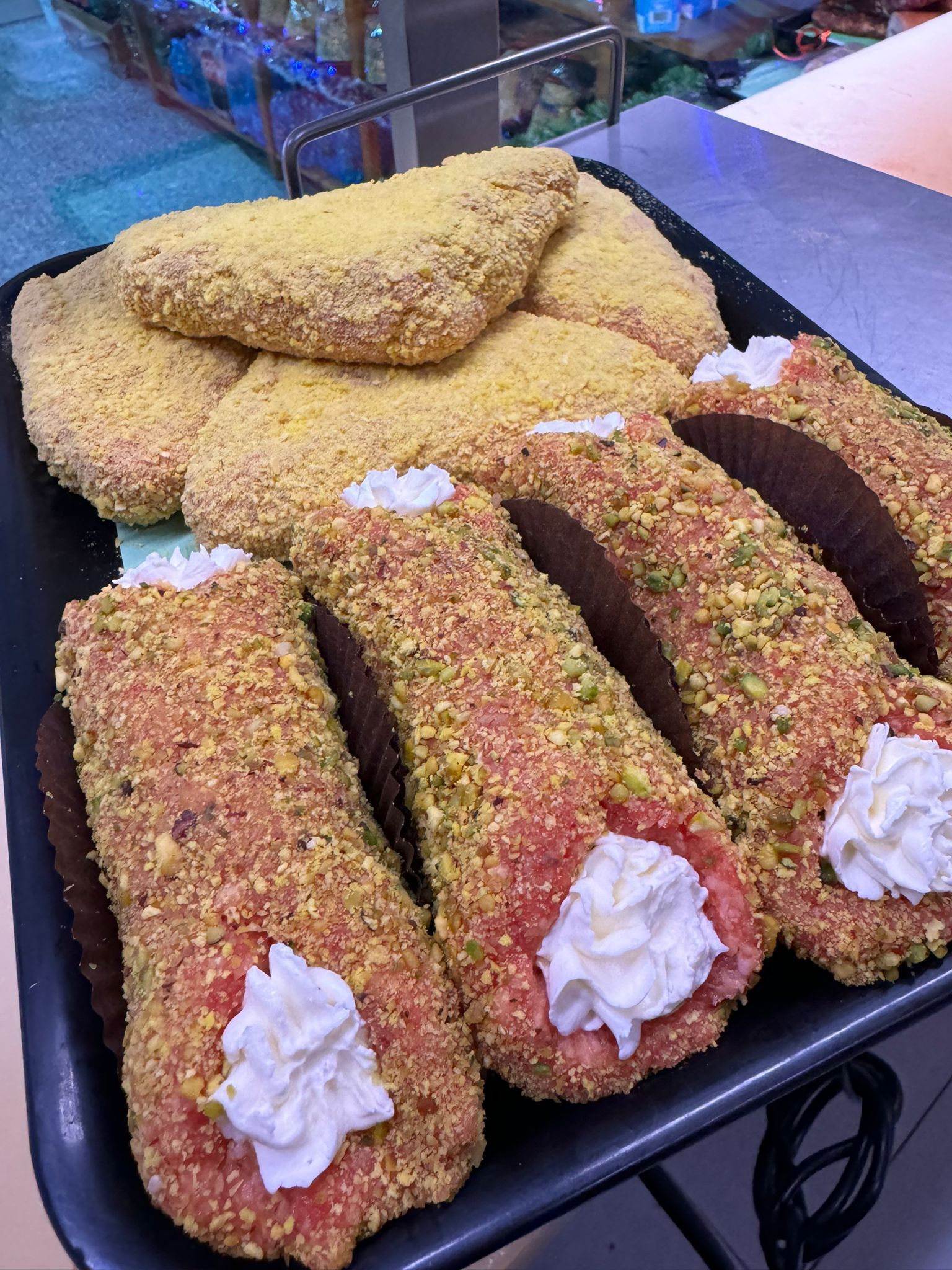 Vassoio di cannoli e biscotti, ricoperti di guarnizioni colorate e ripieni di crema bianca.