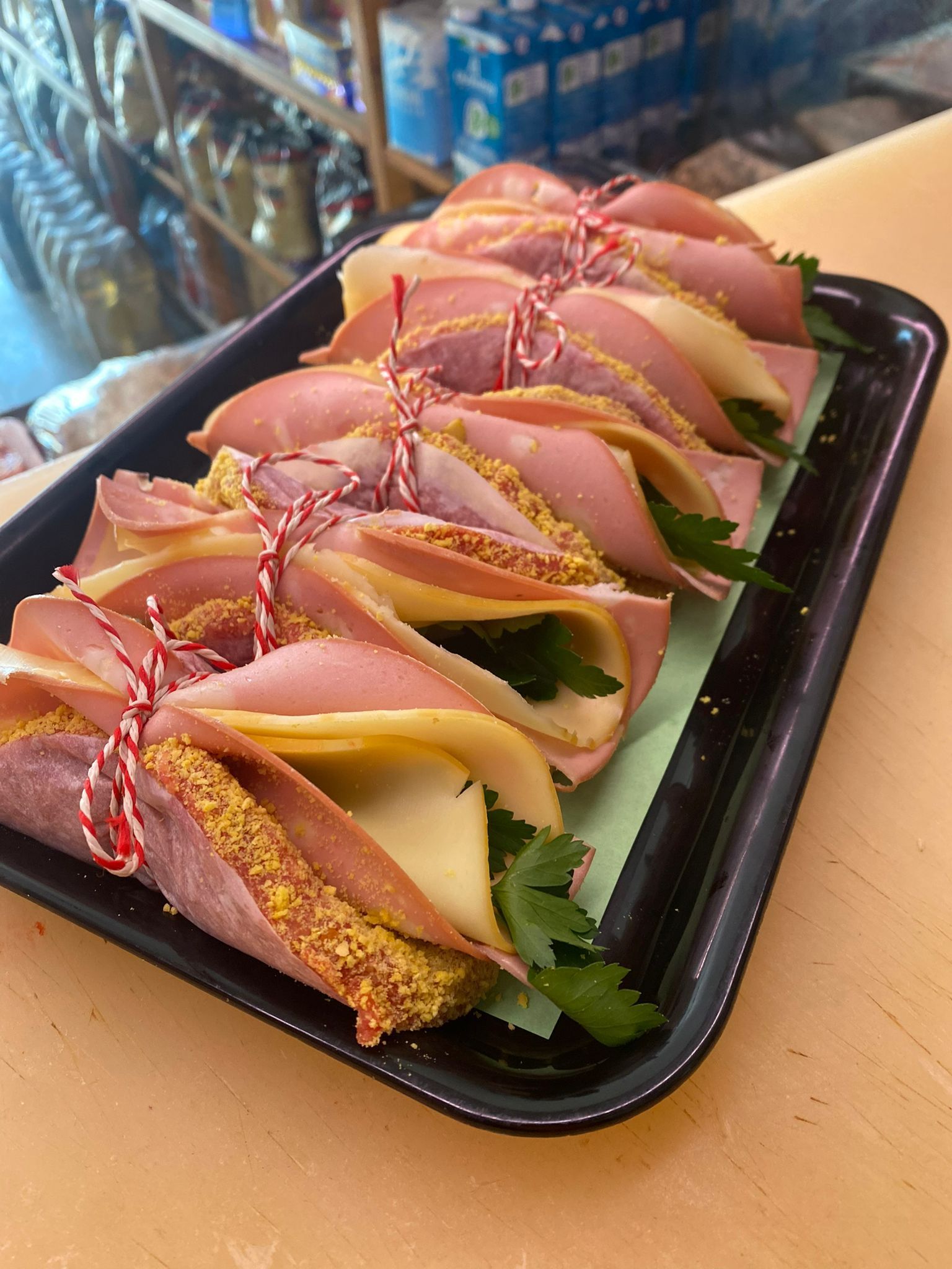 Involtini di prosciutto e formaggio legati con spago su un vassoio nero, guarnito con prezzemolo.