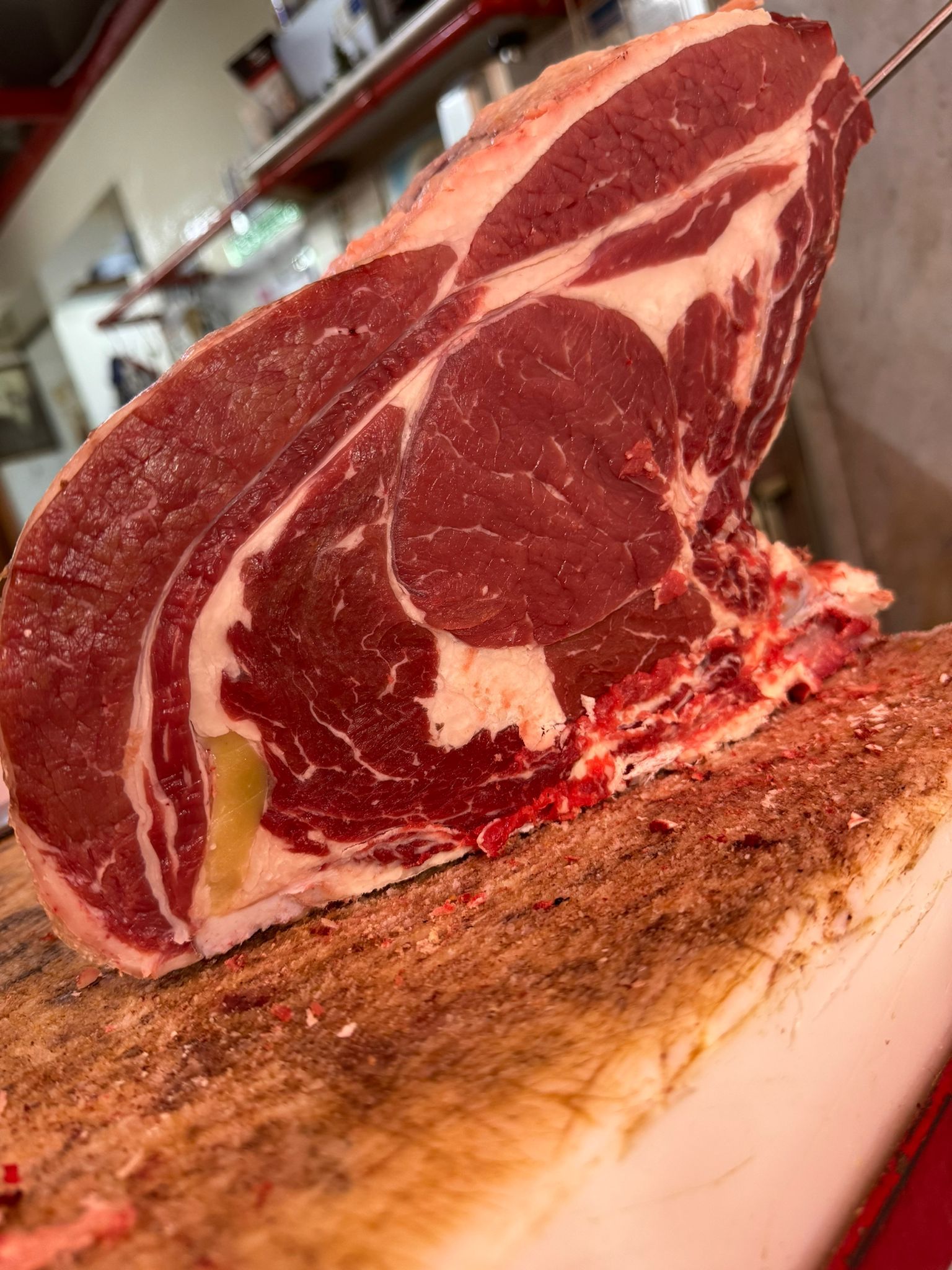 Bistecca di ribeye cruda, tagliata spessa, su un tagliere da macellaio, carne rossa con marezzature bianche, illuminata dall'alto.