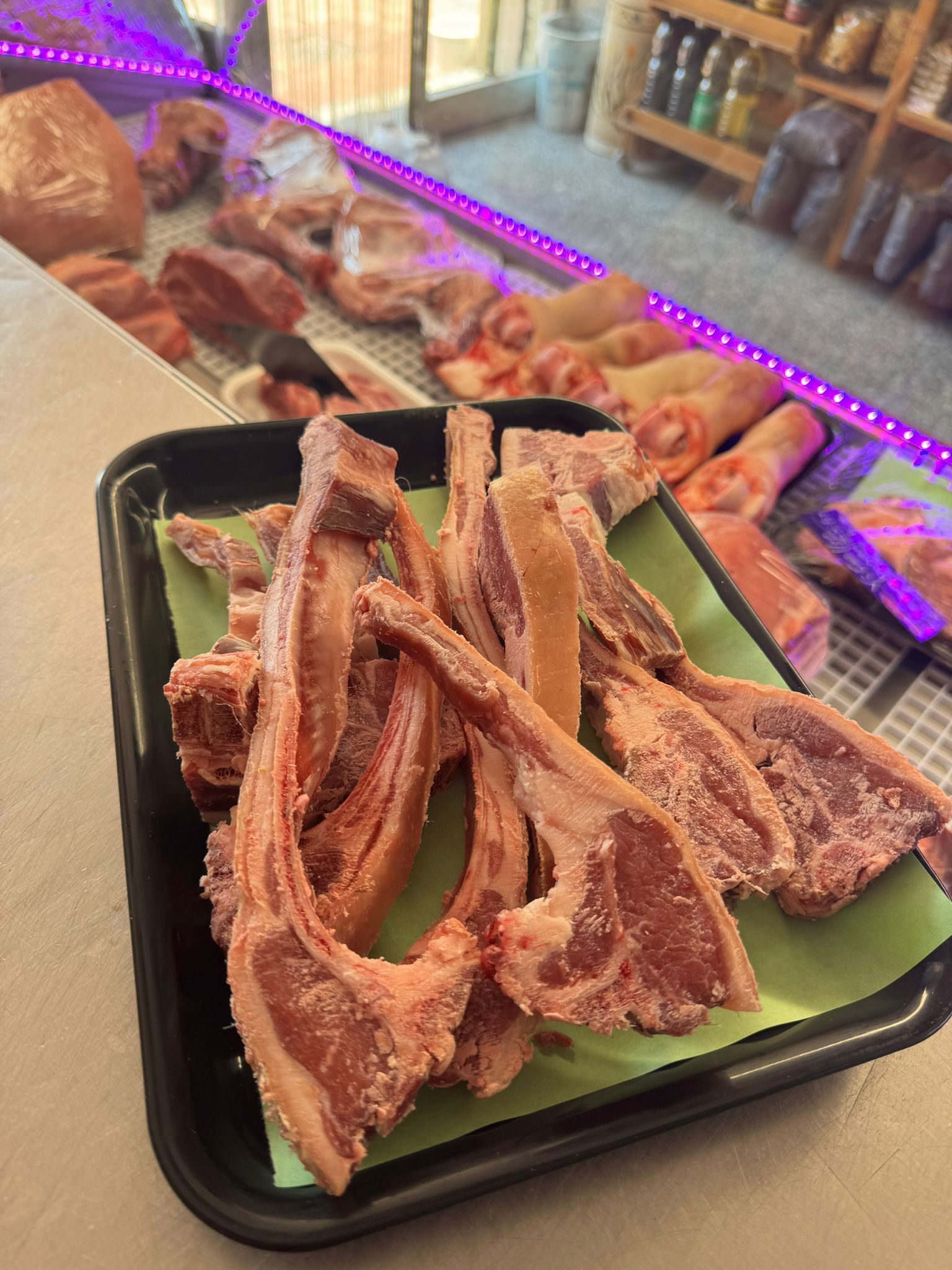 Costolette di agnello su un vassoio, all'interno di una vetrina di macelleria. Altri tagli di carne sono visibili sullo sfondo.