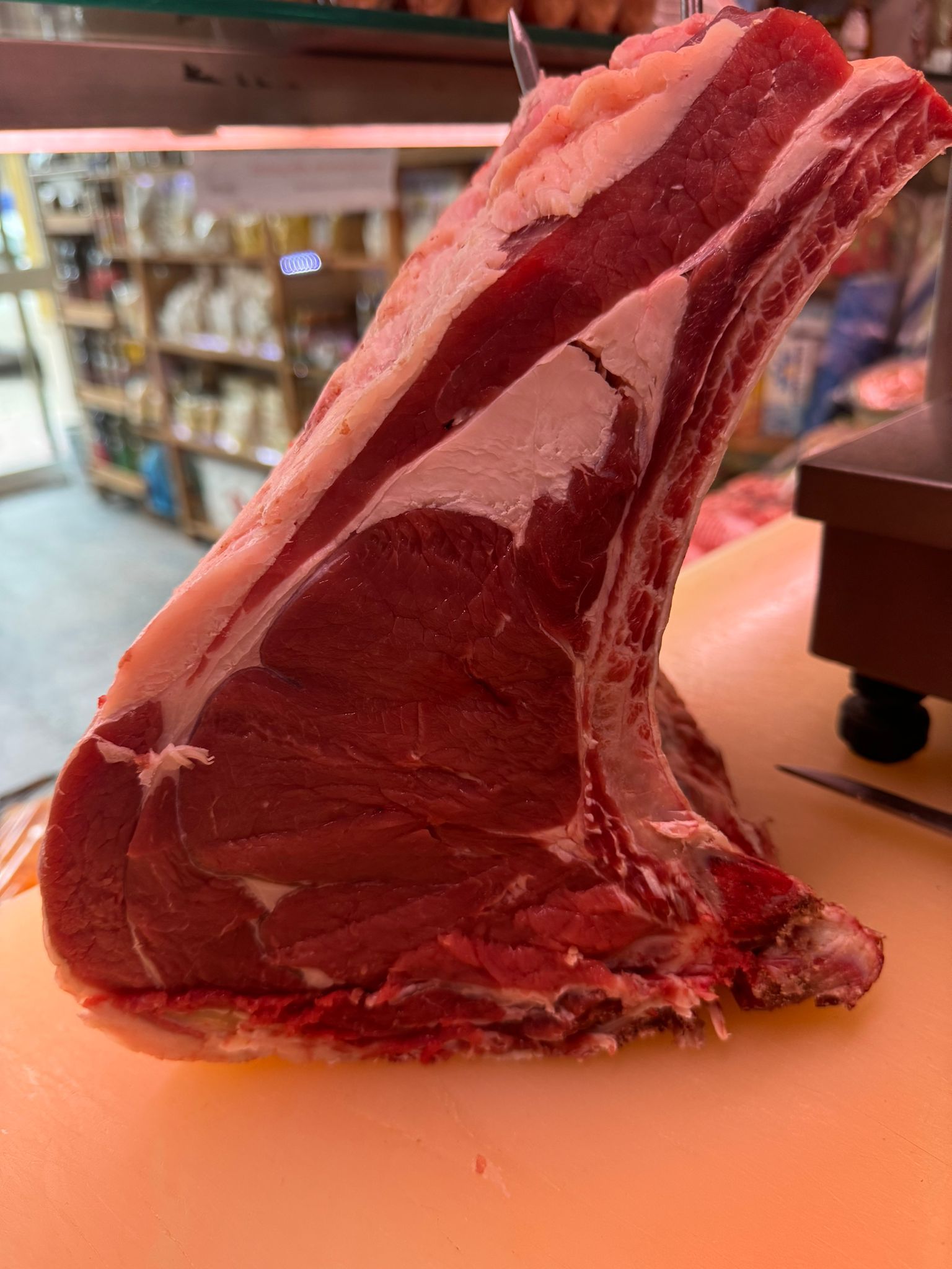 Grande costata di manzo cruda su un tagliere da macellaio. Carne rossa con ossa e grasso, in un ambiente da negozio.