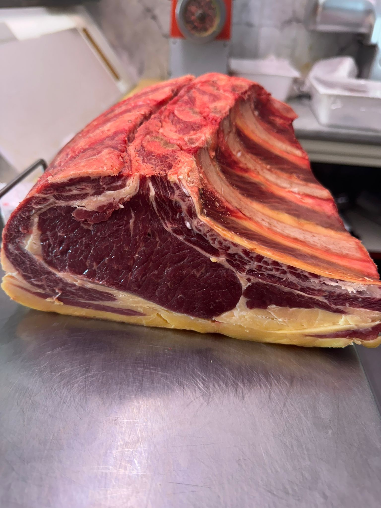 Grande arrosto di costata crudo su una superficie metallica, con venature marmoree e ossa delle costole in evidenza.