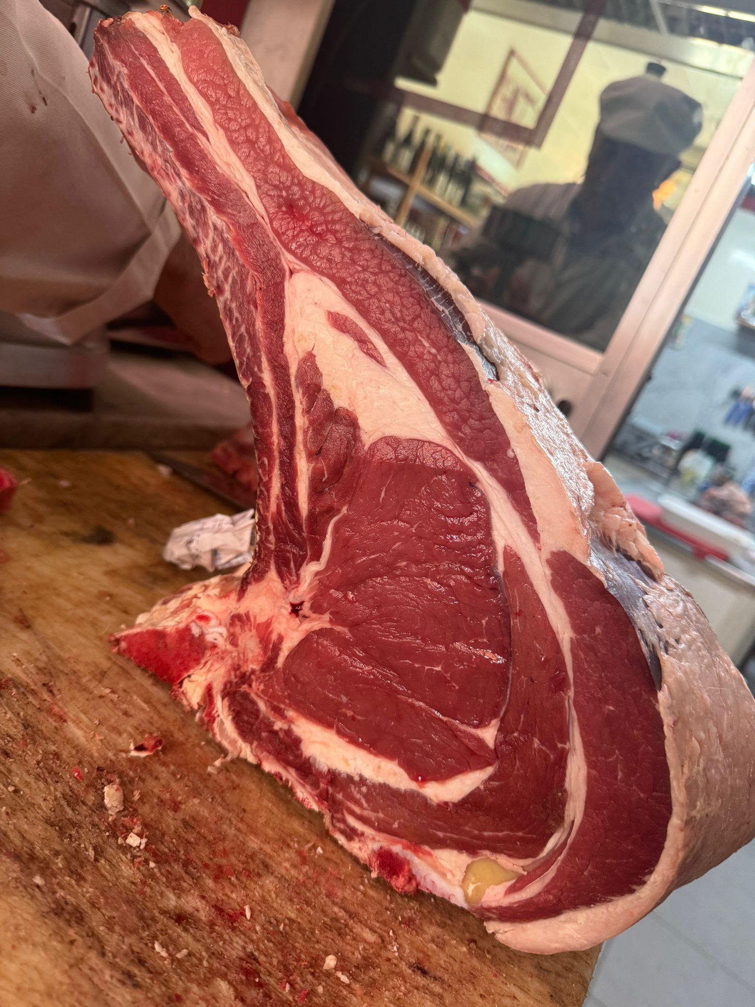 Grande bistecca di ribeye cruda su un tagliere di legno, all'interno di una macelleria.