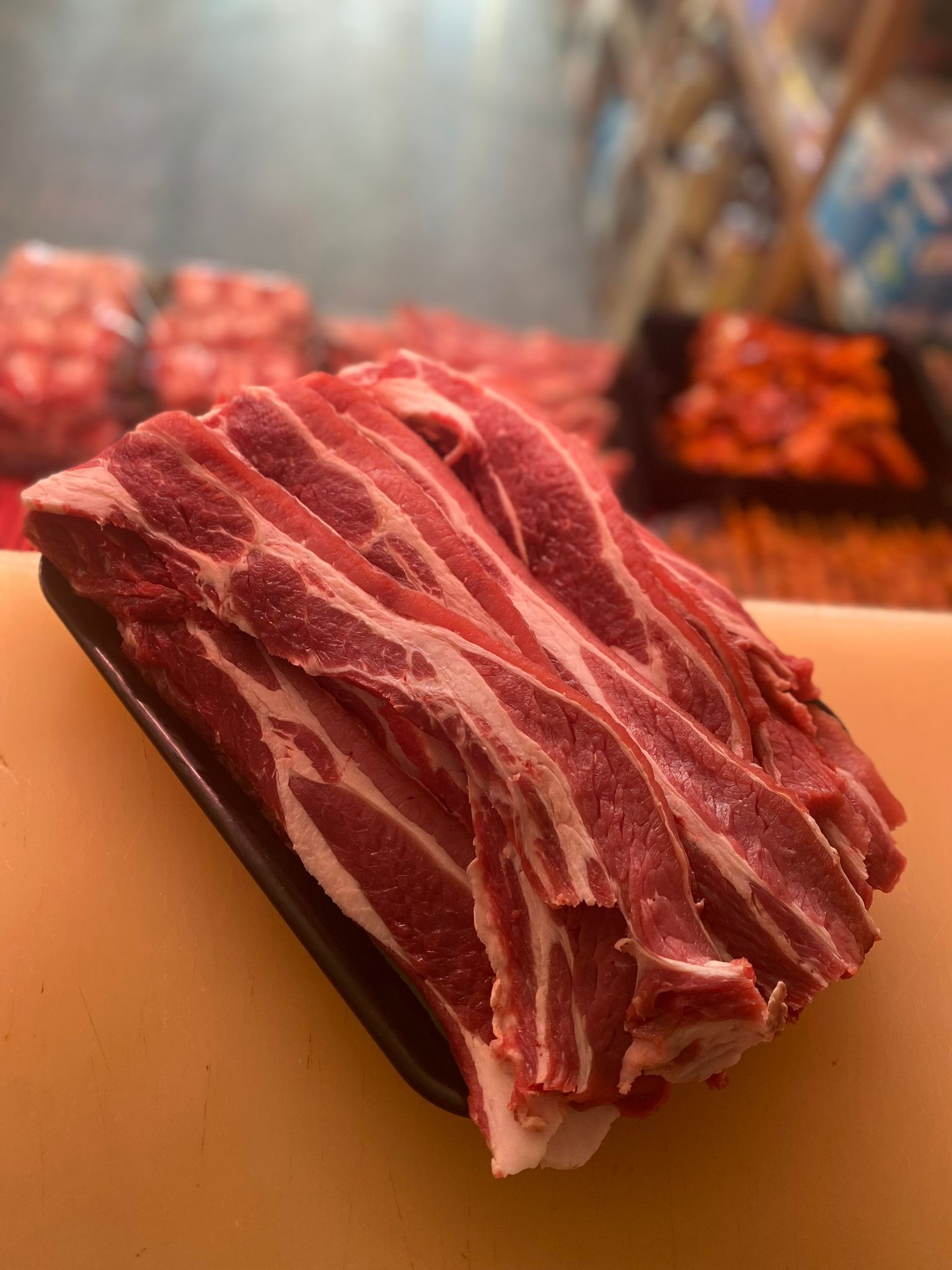 Carne cruda tagliata a fette, rossa con venature bianche, in un vassoio di plastica nera su una superficie gialla.