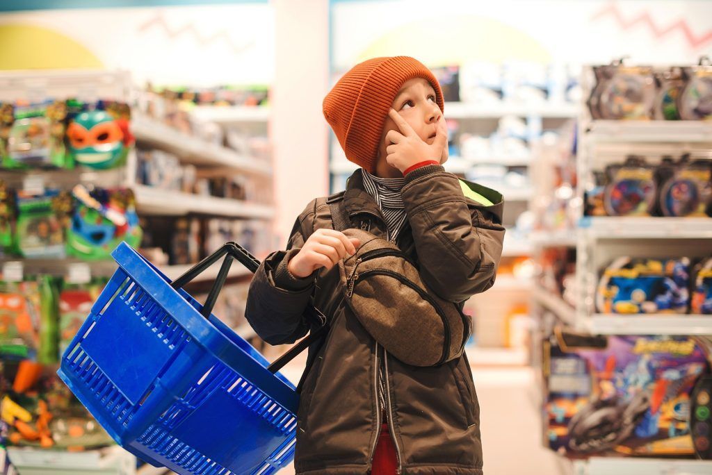 A young boy is holding a shopping basket in a toy store.