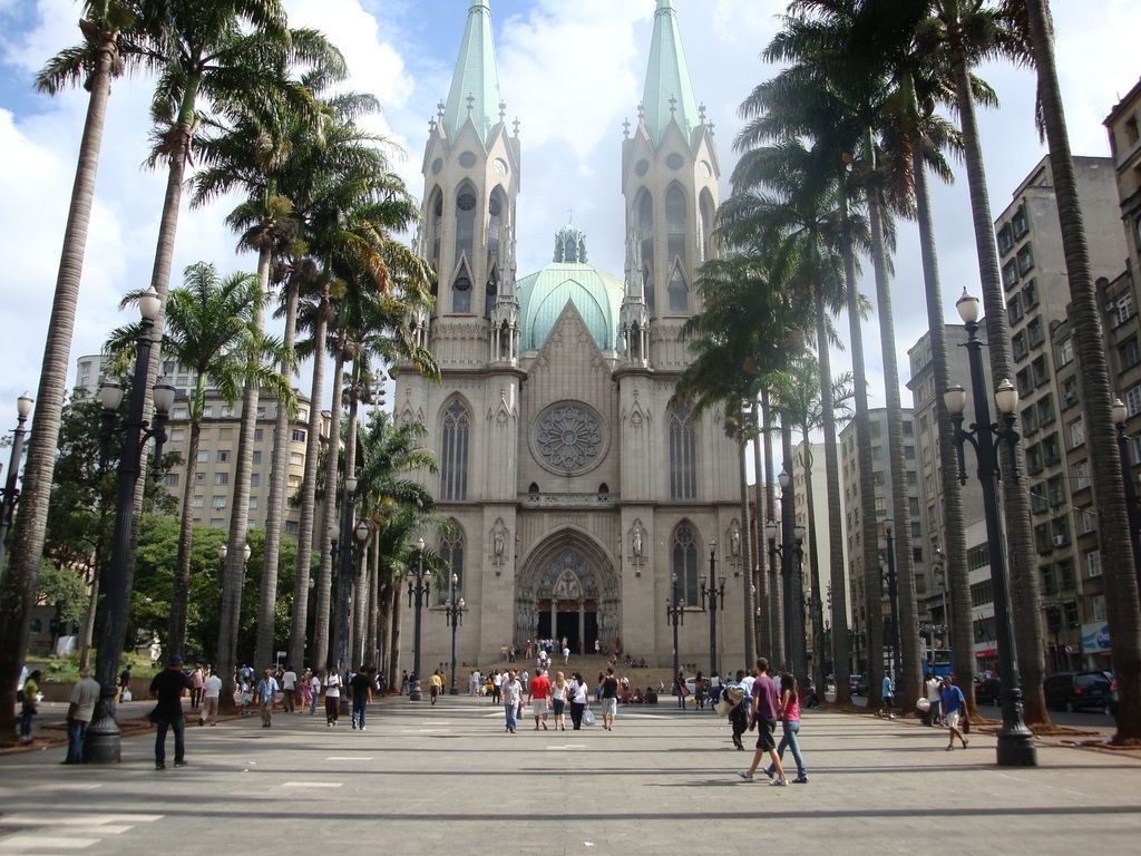 The São Paulo Cathedral in Brazil, a large stone church with twin spires, sits at the end of a palm-lined plaza.