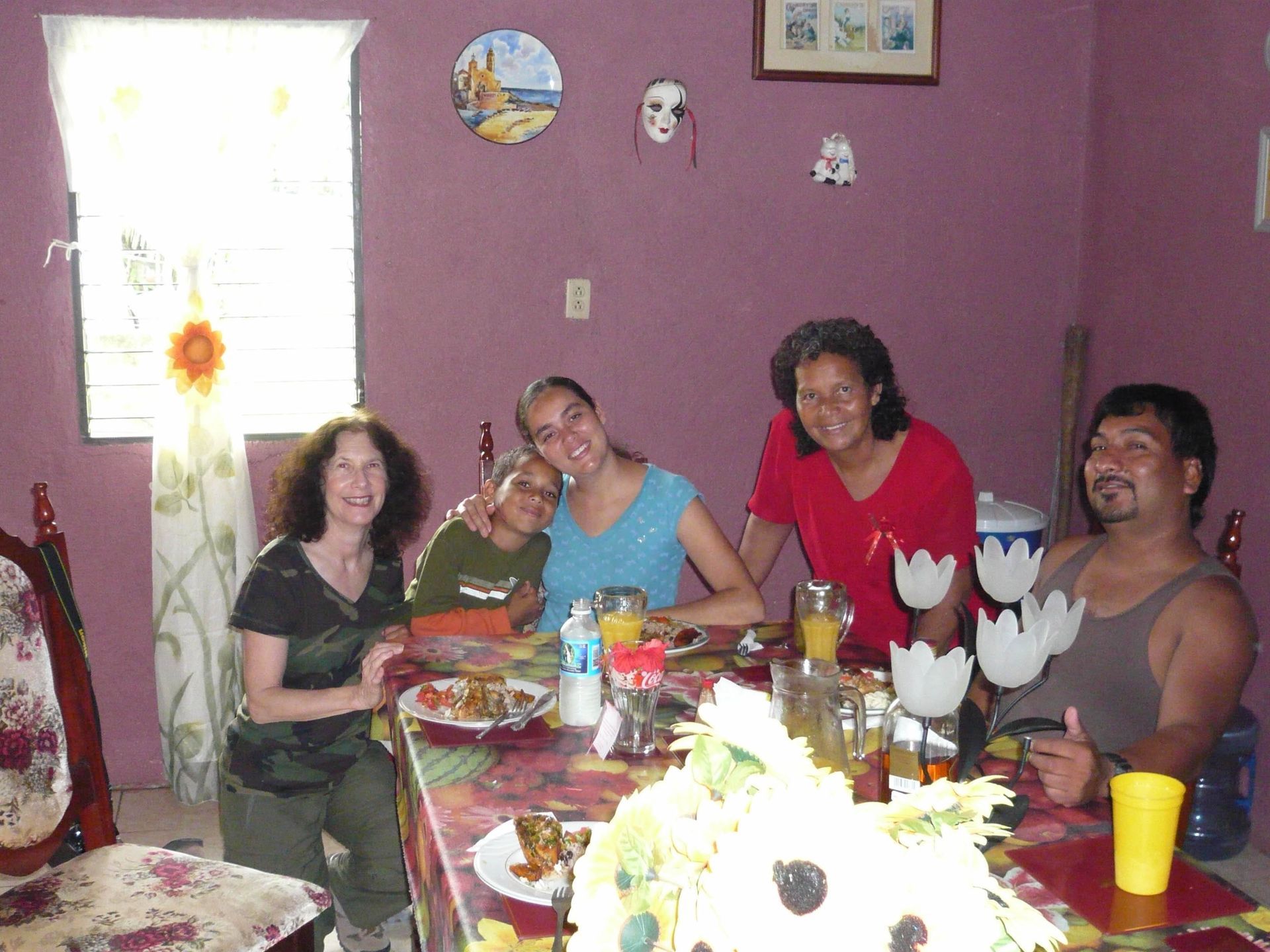 Five people sit around a table in a purple room, smiling and posing for a photo while eating a meal.