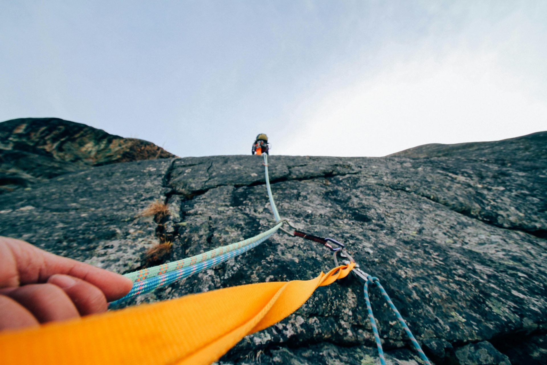 First-person view of a person rock climbing on a grey stone face, holding a bright yellow climbing sling with ropes ahead.