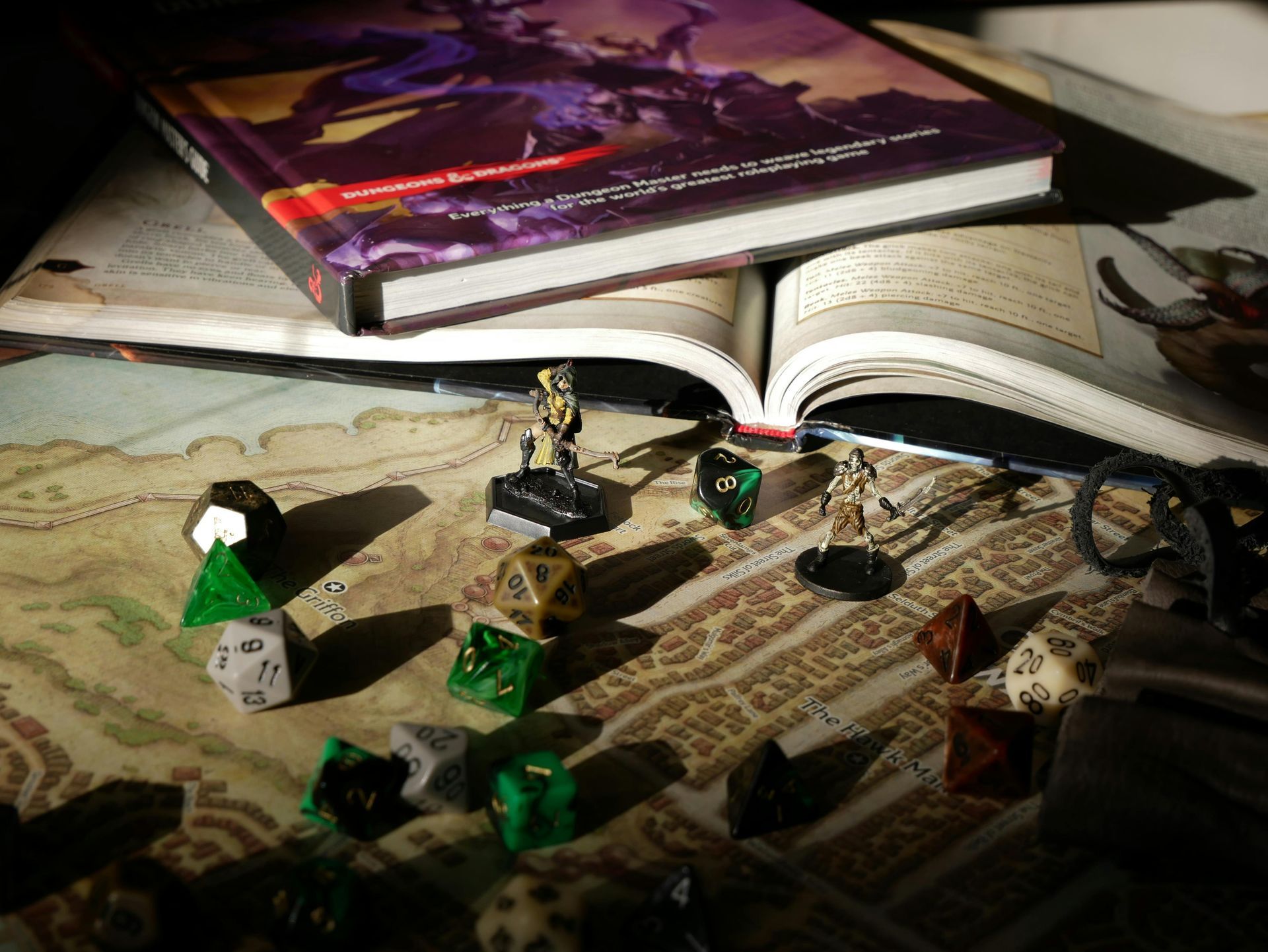 Dungeons & Dragons tabletop gaming setup with a rulebook, miniature figures, and scattered polyhedral dice on a map.