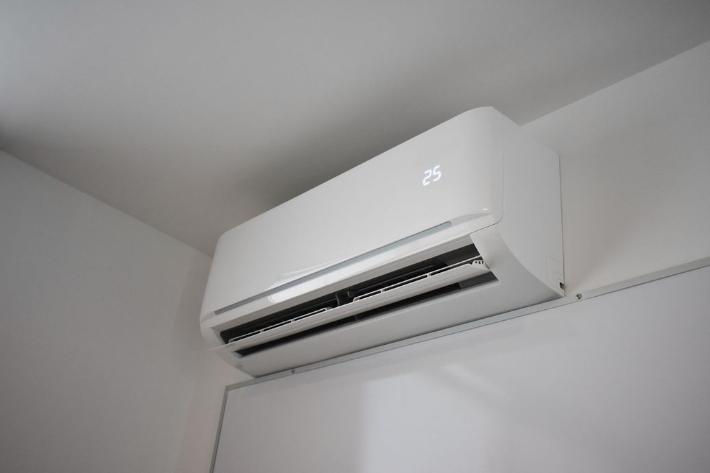 White wall-mounted air conditioner installed near the ceiling in a room corner.