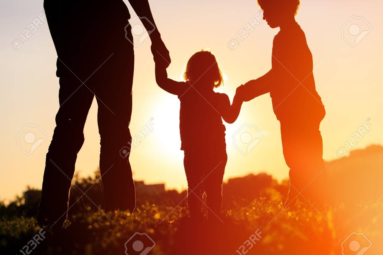 A man and two children are holding hands at sunset.