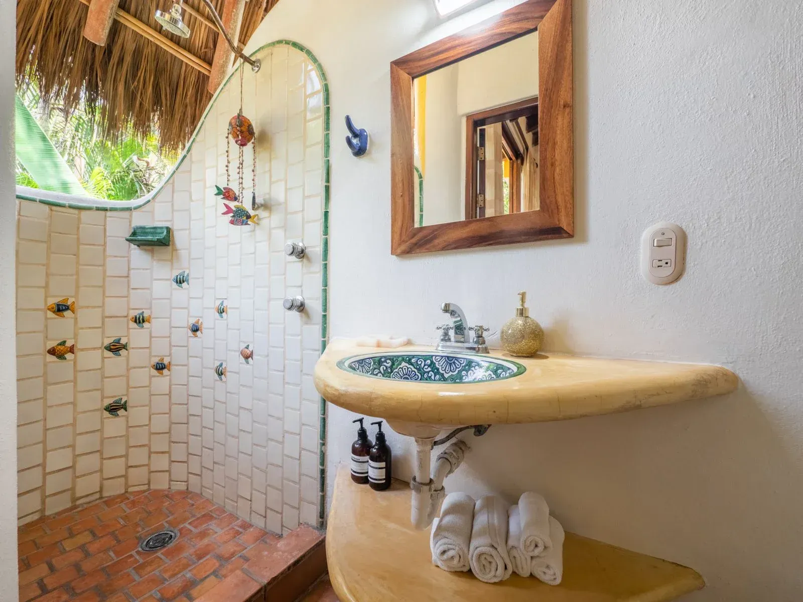 Bathroom with a tiled shower, curved sink, wooden mirror, and thatched roof detail.