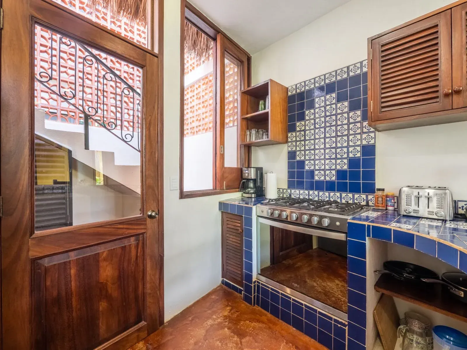 Kitchen with blue tile, wooden cabinets, and a gas stove. Stairs visible through a glass door.