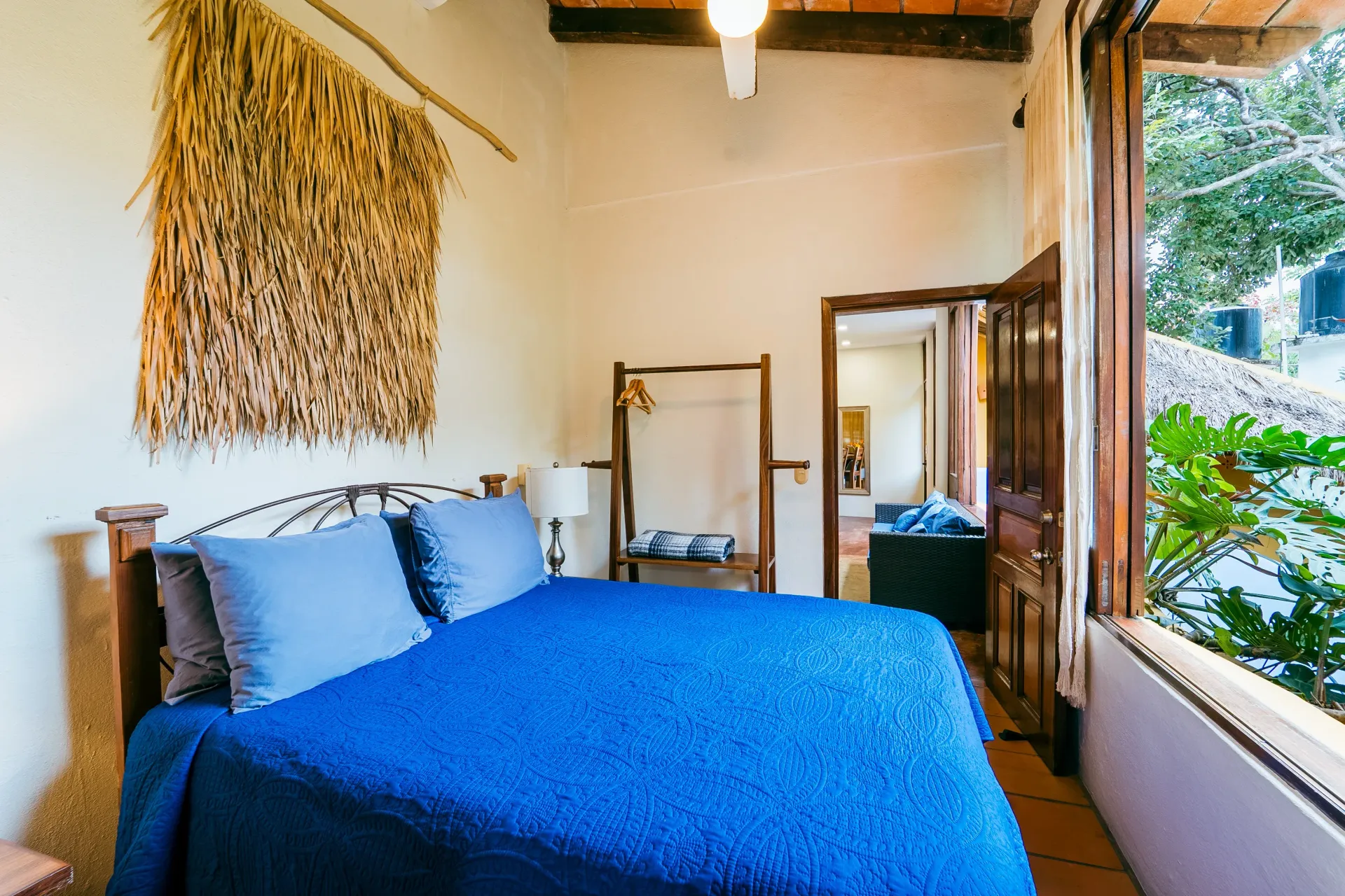 Bedroom with blue bed, natural wall decor, open door to balcony with greenery.