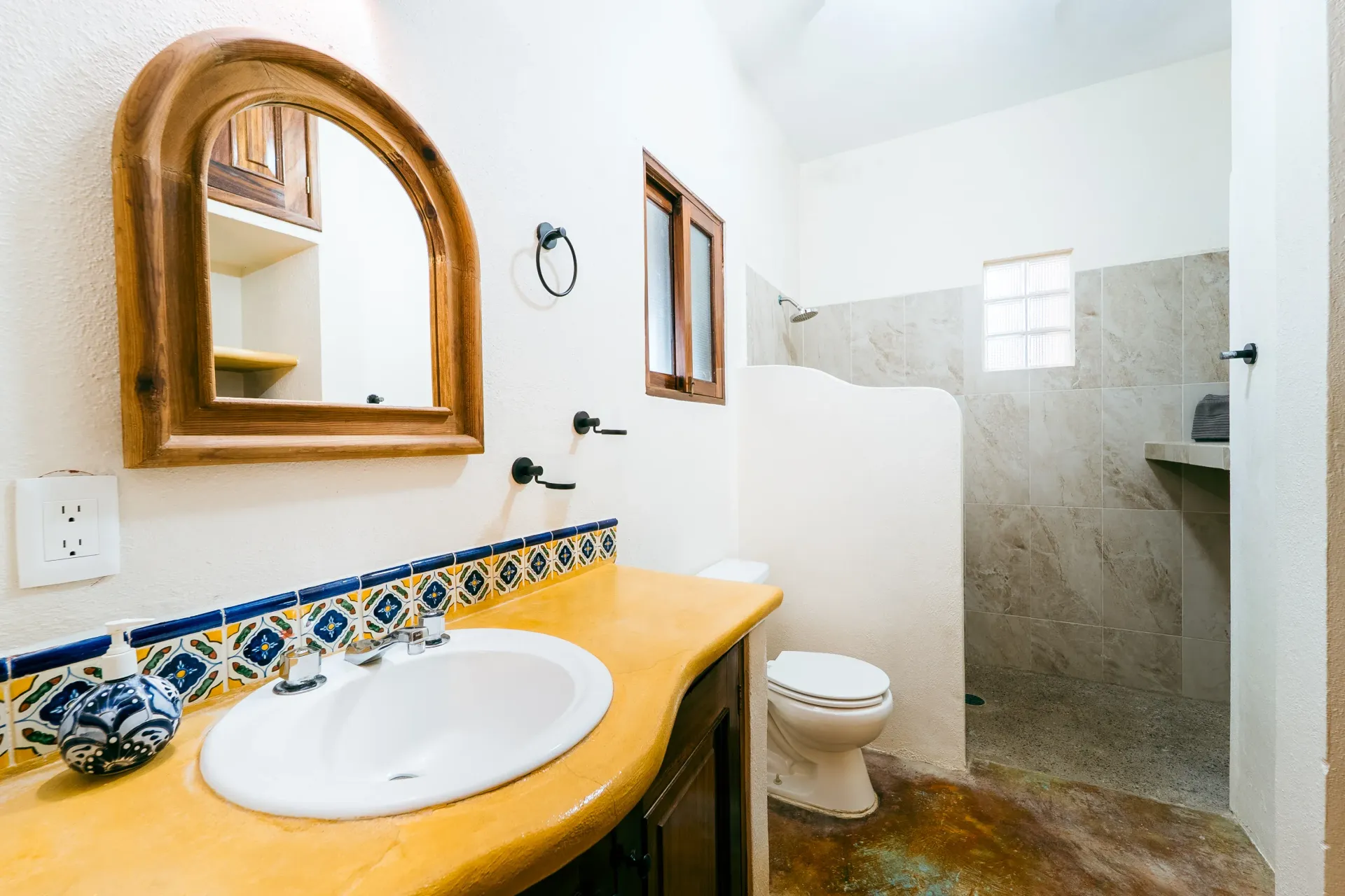 Bathroom with a sink, toilet, and shower. Yellow countertop, blue tile, and a wooden mirror frame.