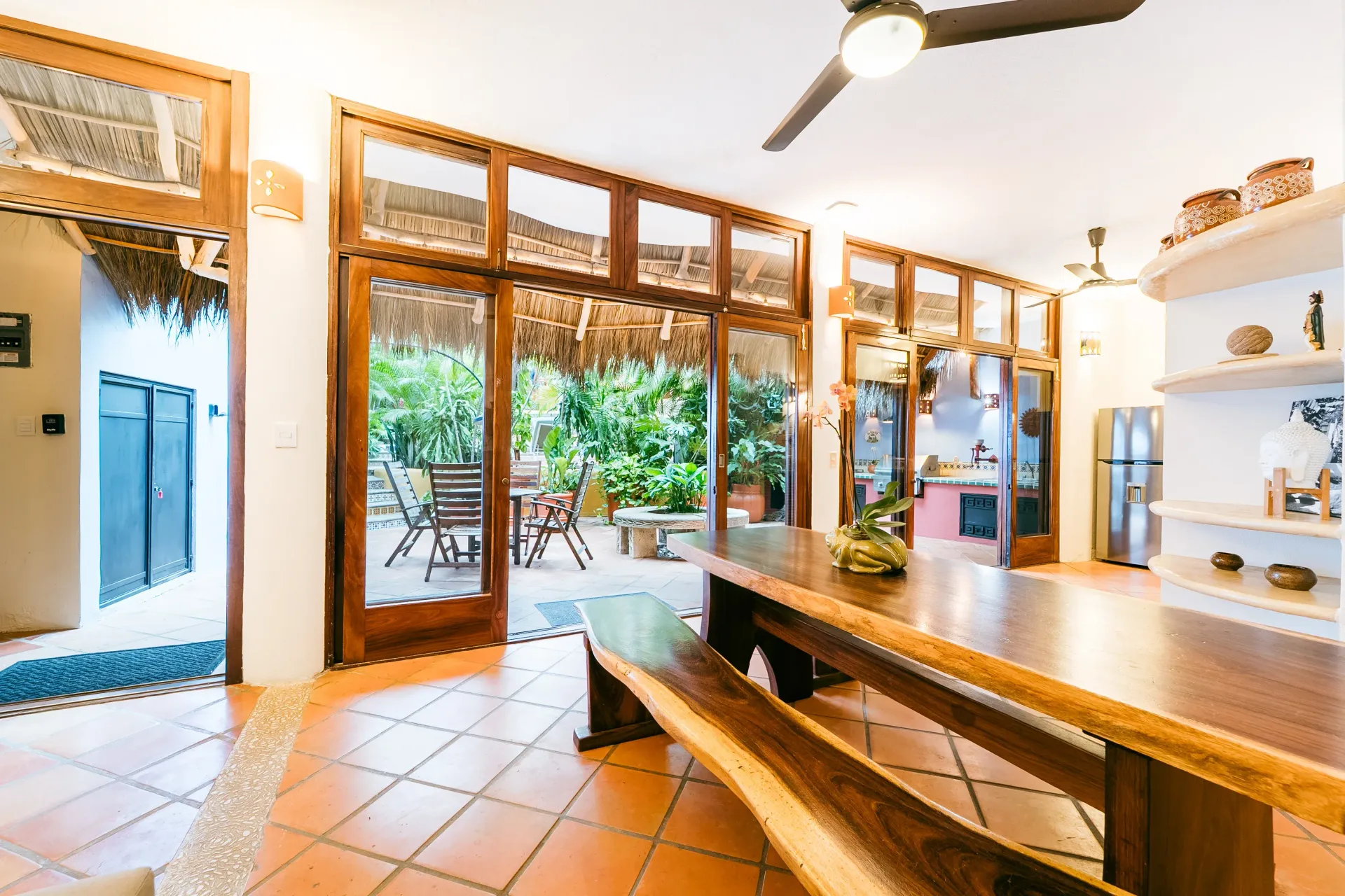 Open-air kitchen with wooden table, glass doors to patio, and rustic roof.