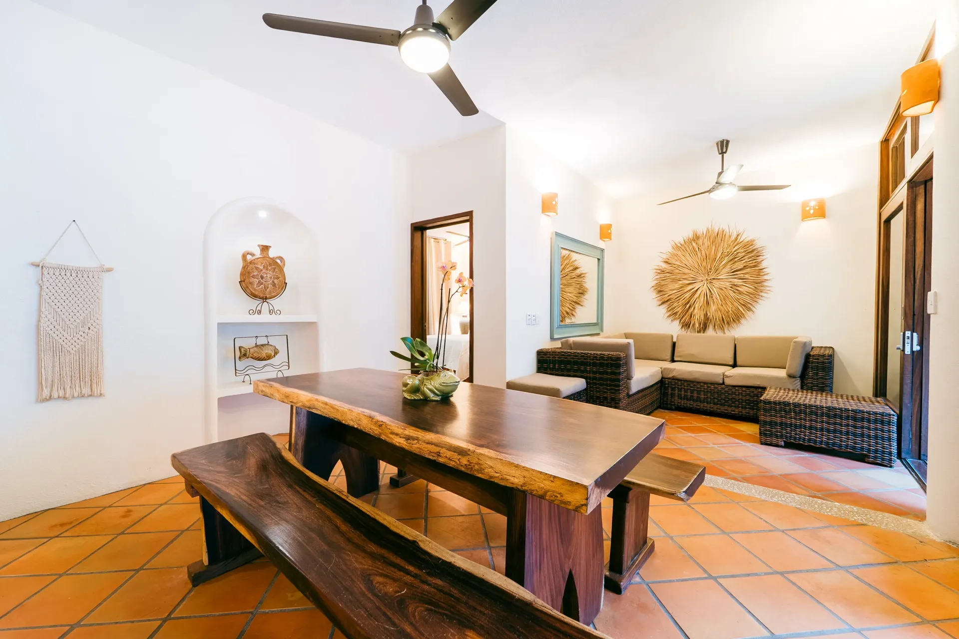 Dining room with rustic wooden table and benches, connecting to a living area with a sofa.