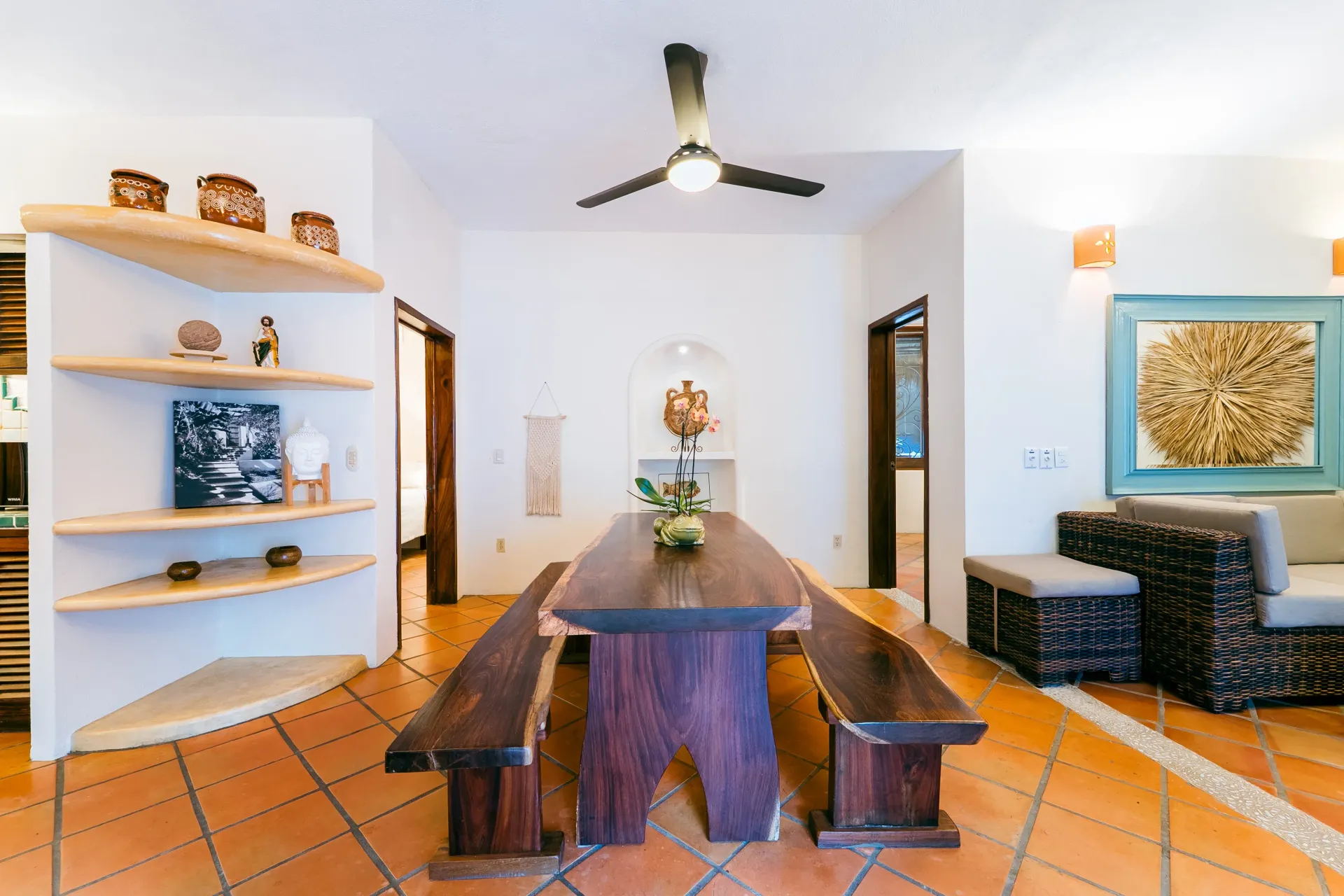 Spacious dining area with long wooden table and benches. Terracotta tile floors, white walls, and built-in shelves.