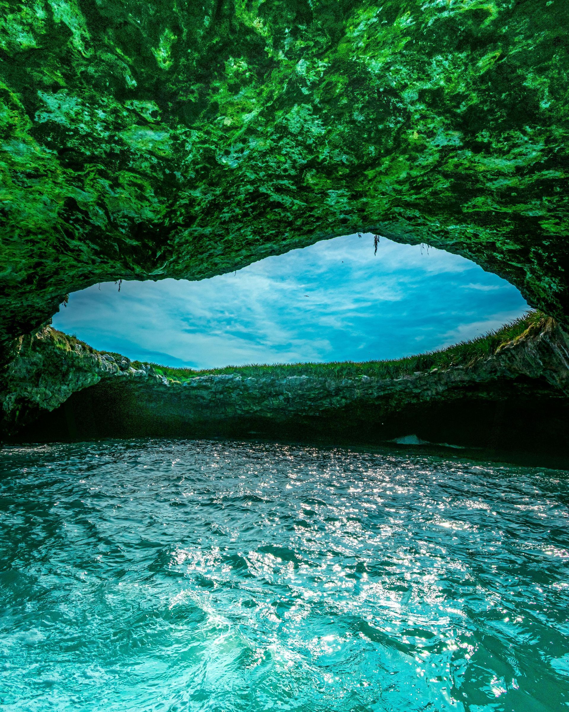 Cave opening to the sky above turquoise water. Sunlight reflects 