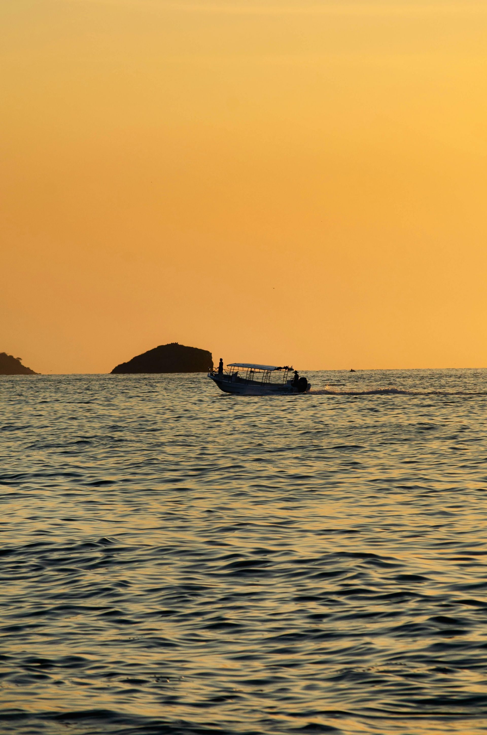 Boat on water at sunset with small island in the background. Orange sky.