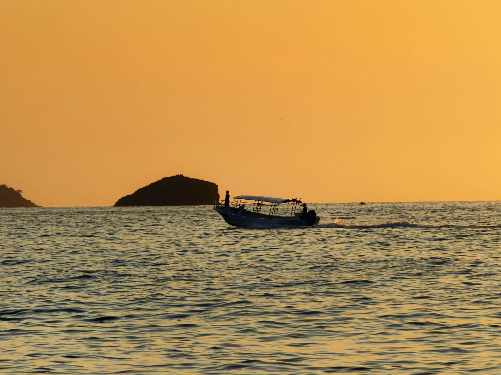Boat on water at sunset, silhouetted against an orange sky. Island in background.