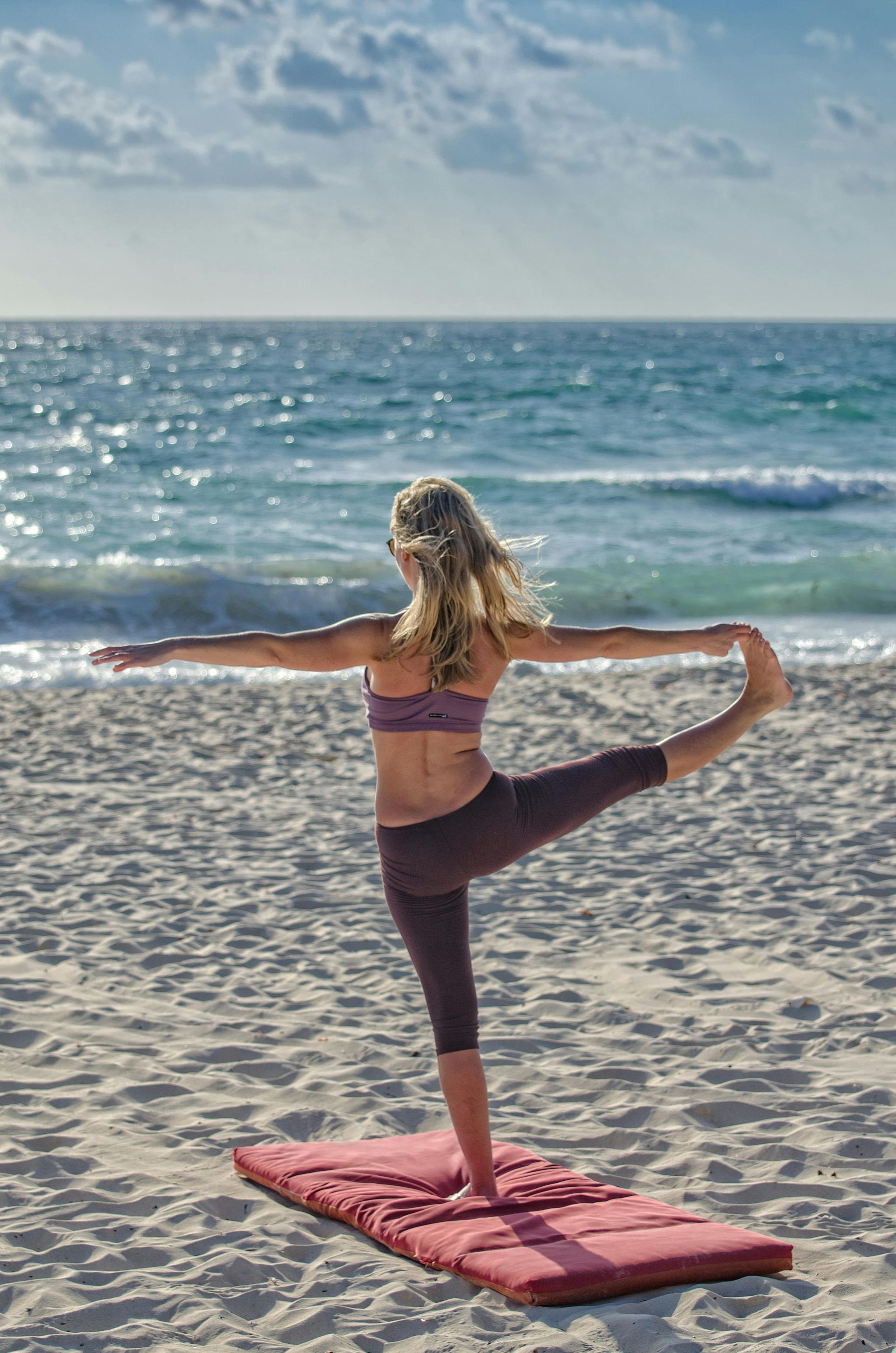 Woman in yoga pose on beach, arms outstretched, leg raised.
