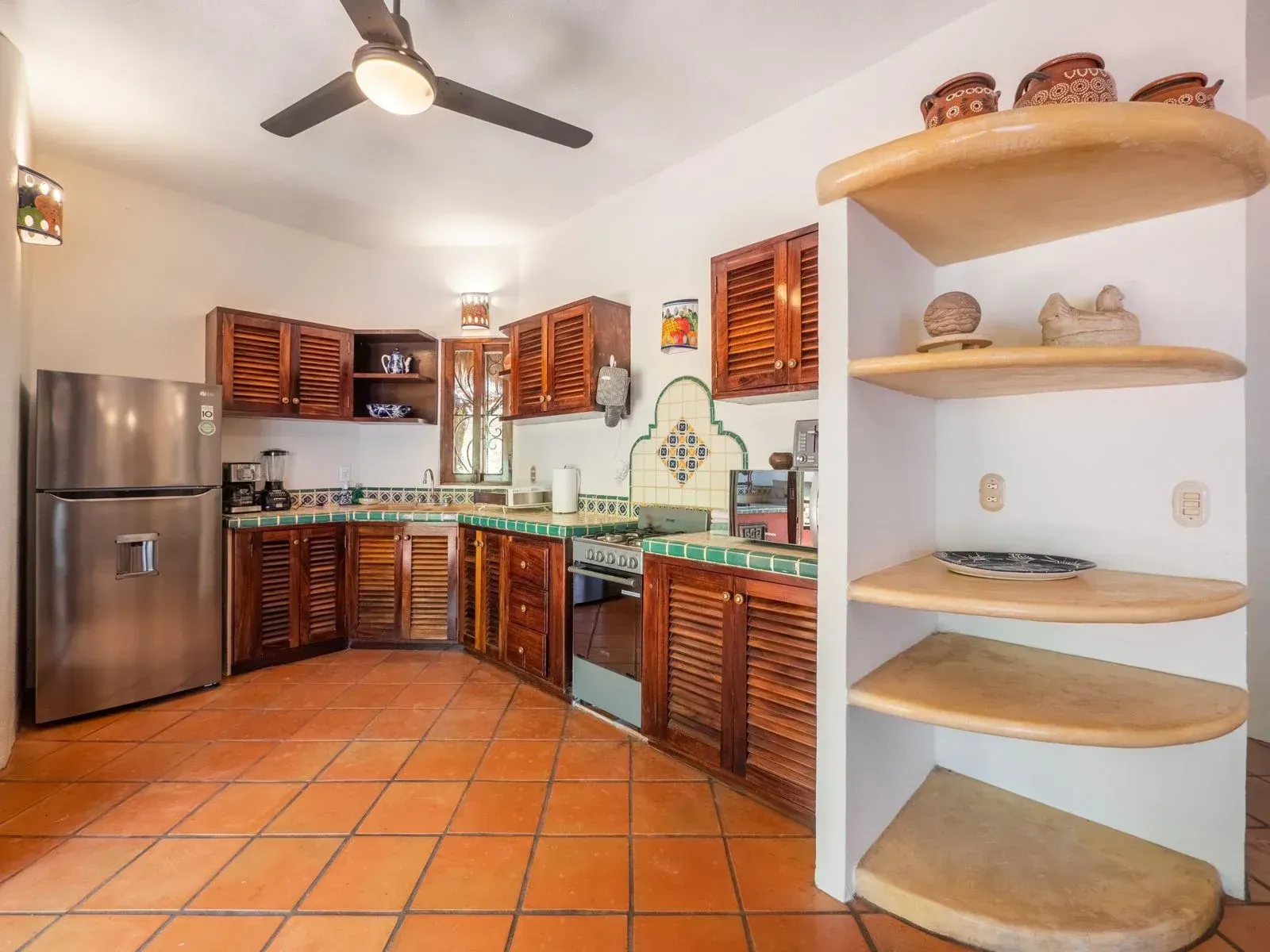 Kitchen with brown wooden cabinets, stainless steel refrigerator, and terracotta tile floor.