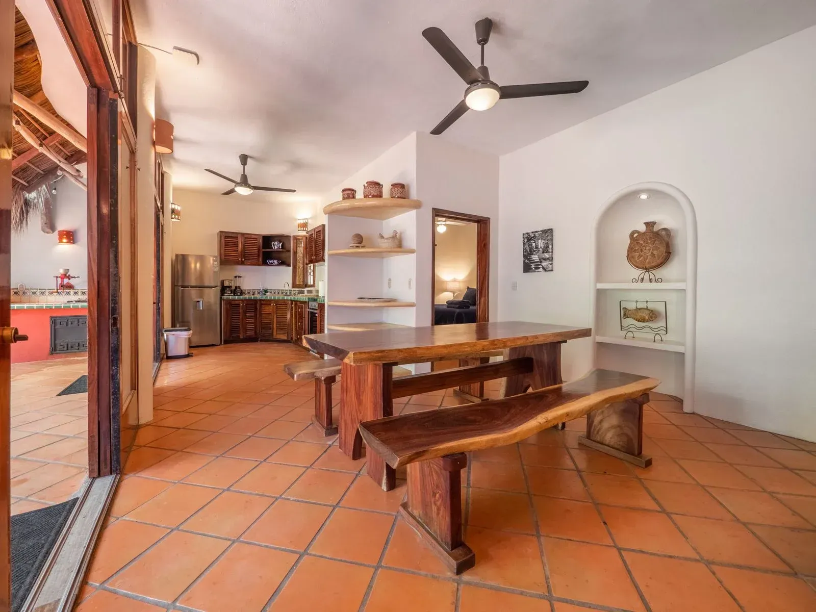 Dining area with a large wooden table, benches, and a kitchen visible in the background.