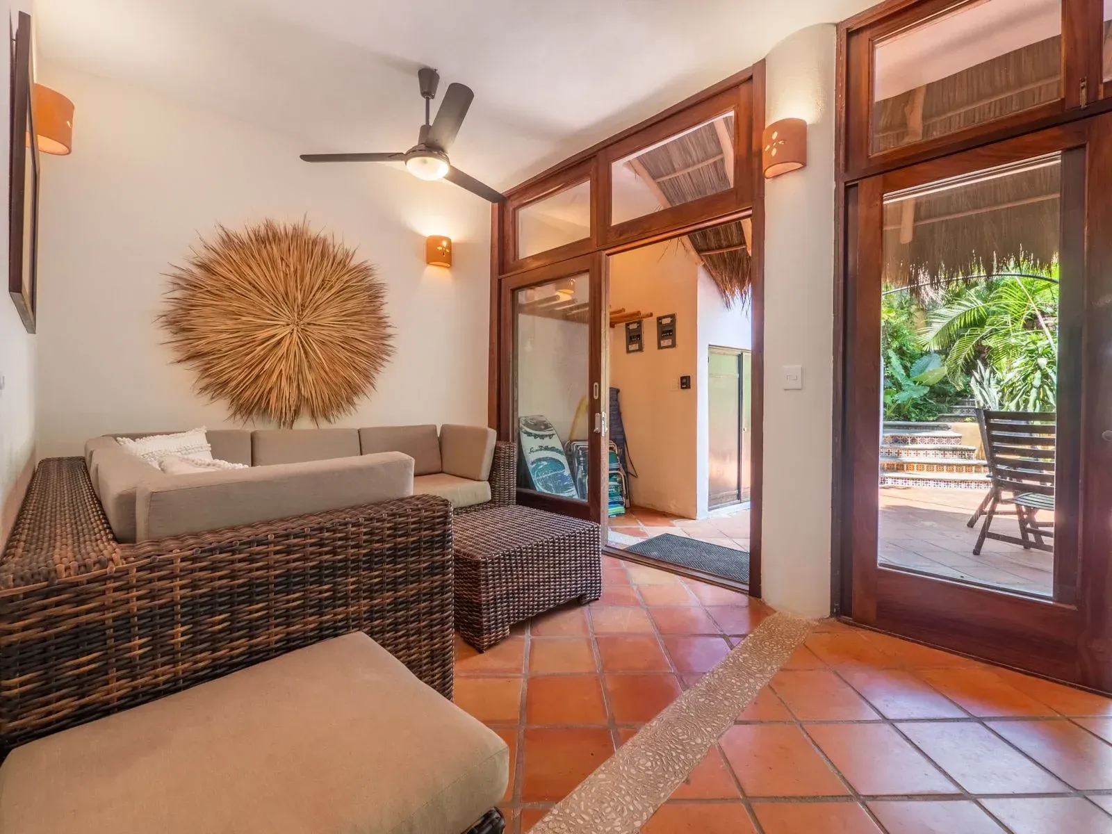 Living room with brown tile floor, wicker furniture, and large glass doors leading to a patio.