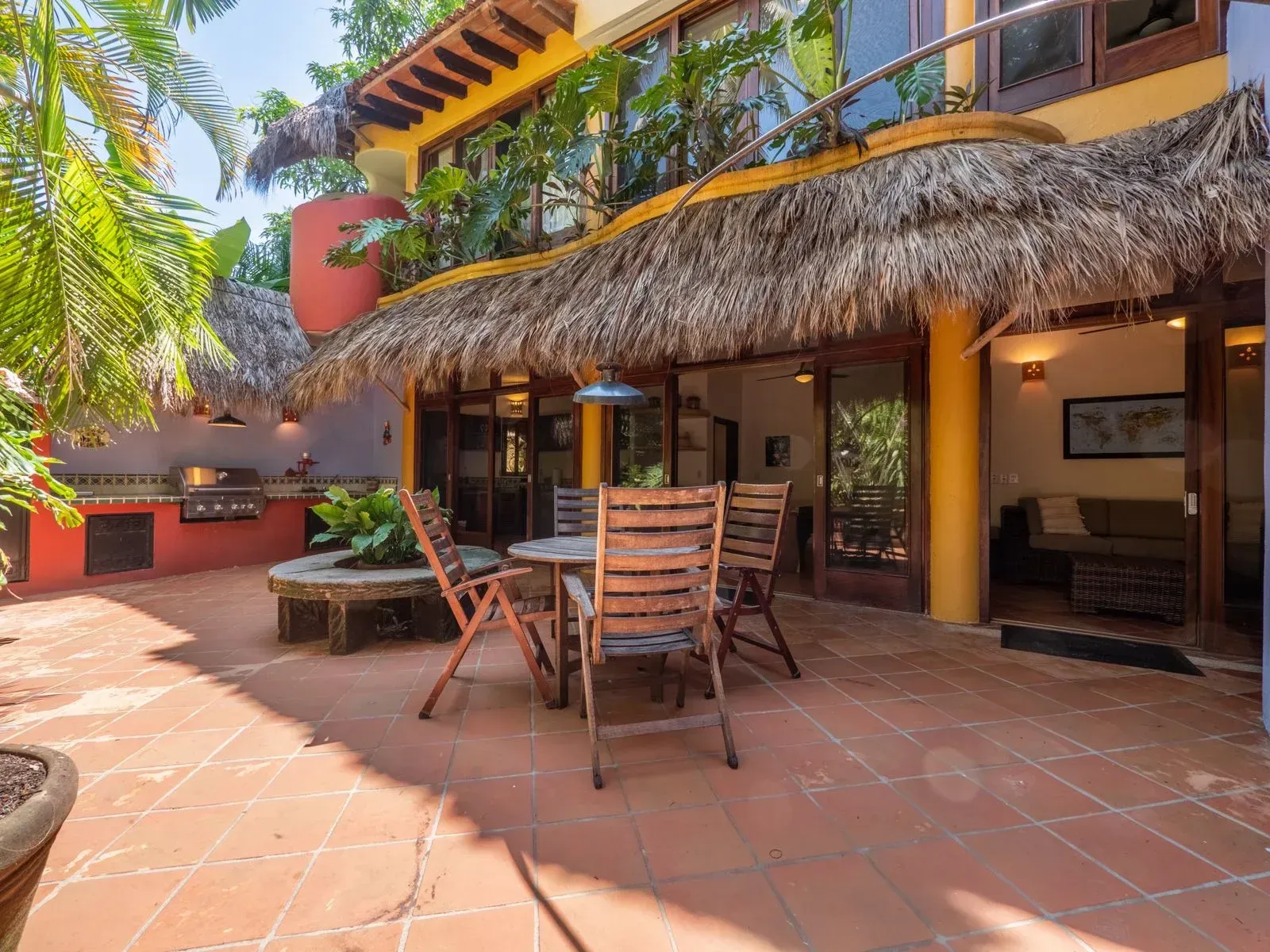 Outdoor patio with dining set, grill, and thatched roof, adjacent to a home.