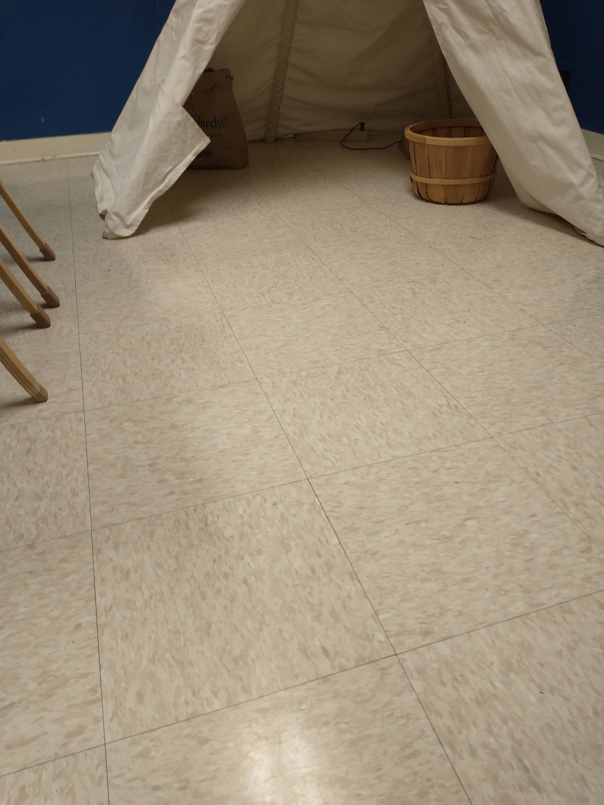 Canvas tent in a room with a basket and folding chair on a tiled floor