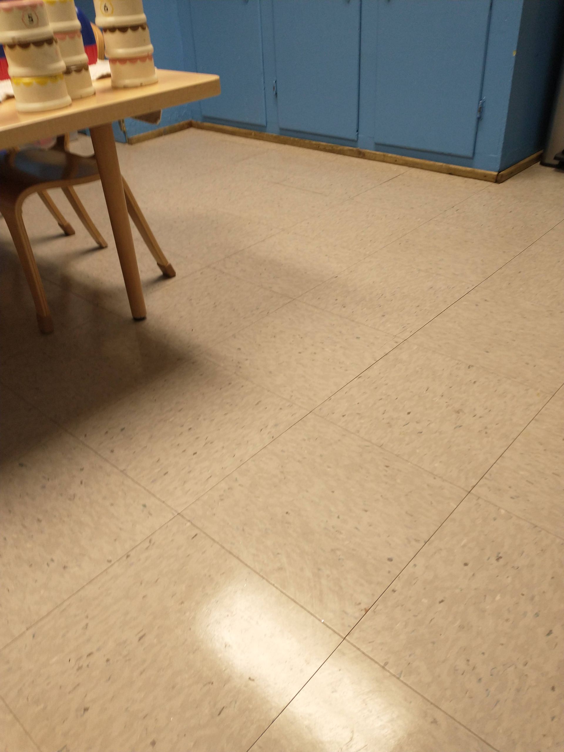 Empty classroom floor with blue cabinets and a table with stools on the left.