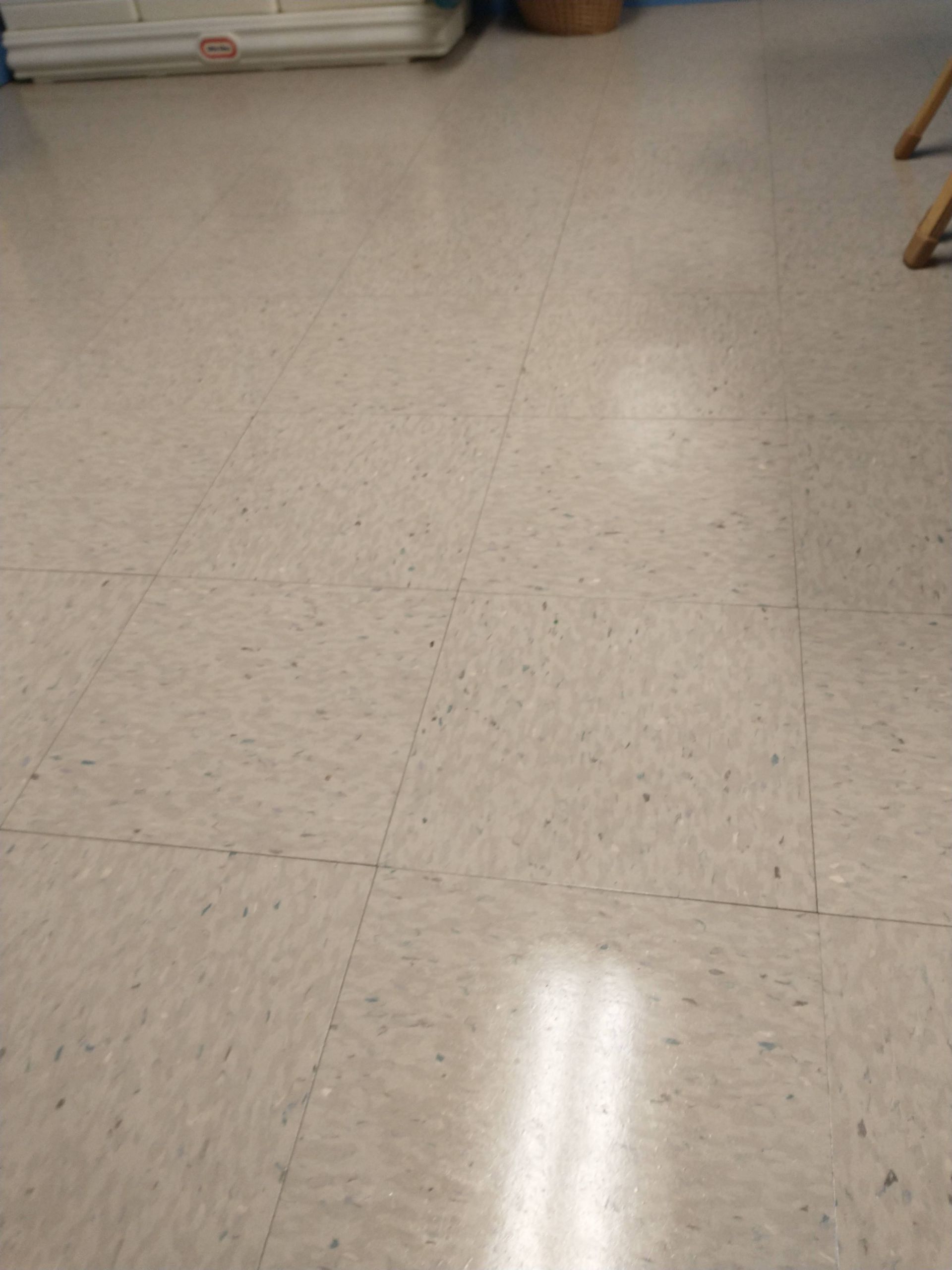 Empty beige tiled floor with reflections from overhead lights and a chair leg at the right edge