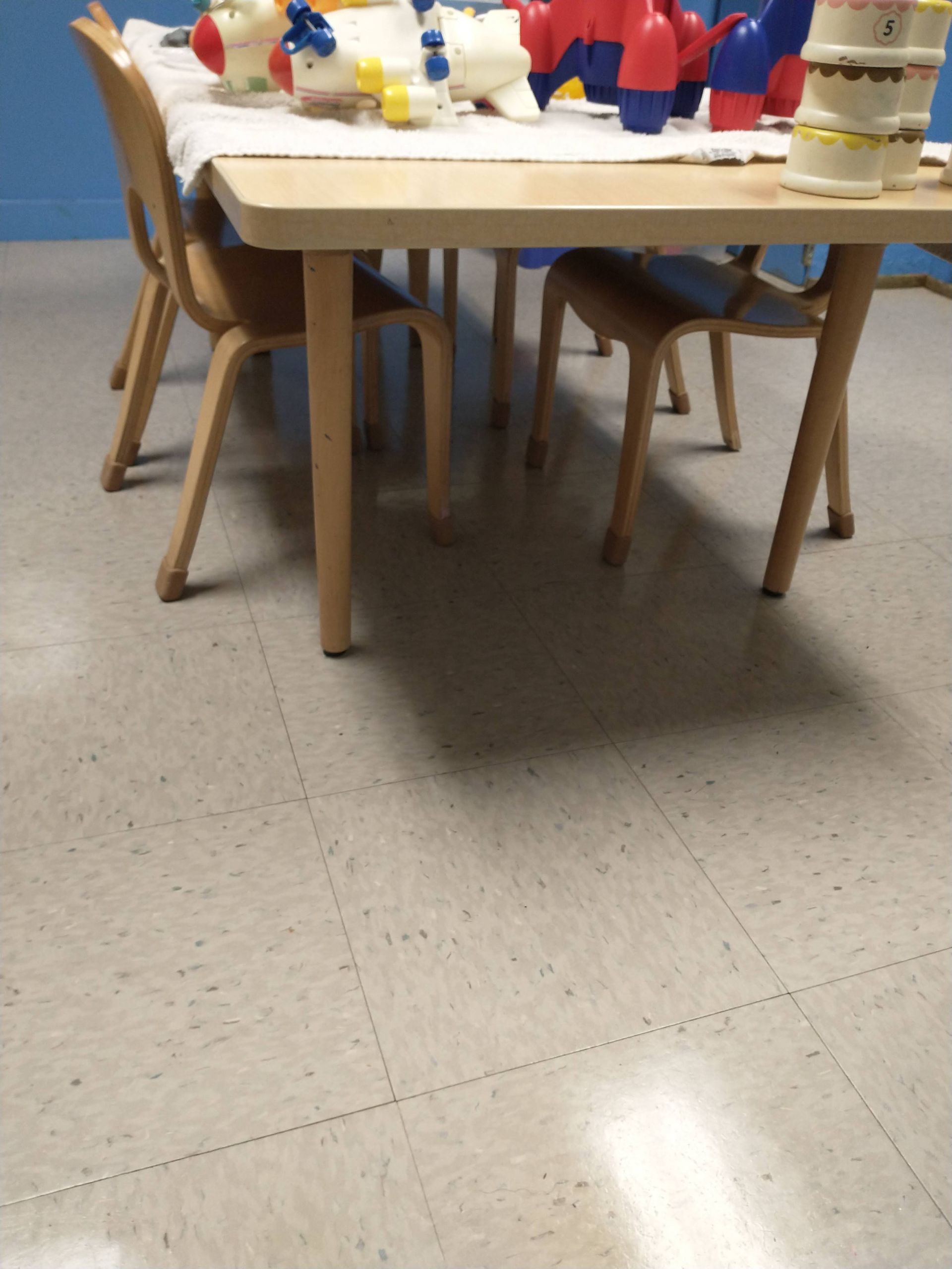 Children seated at a table with toys in a classroom on a tiled floor